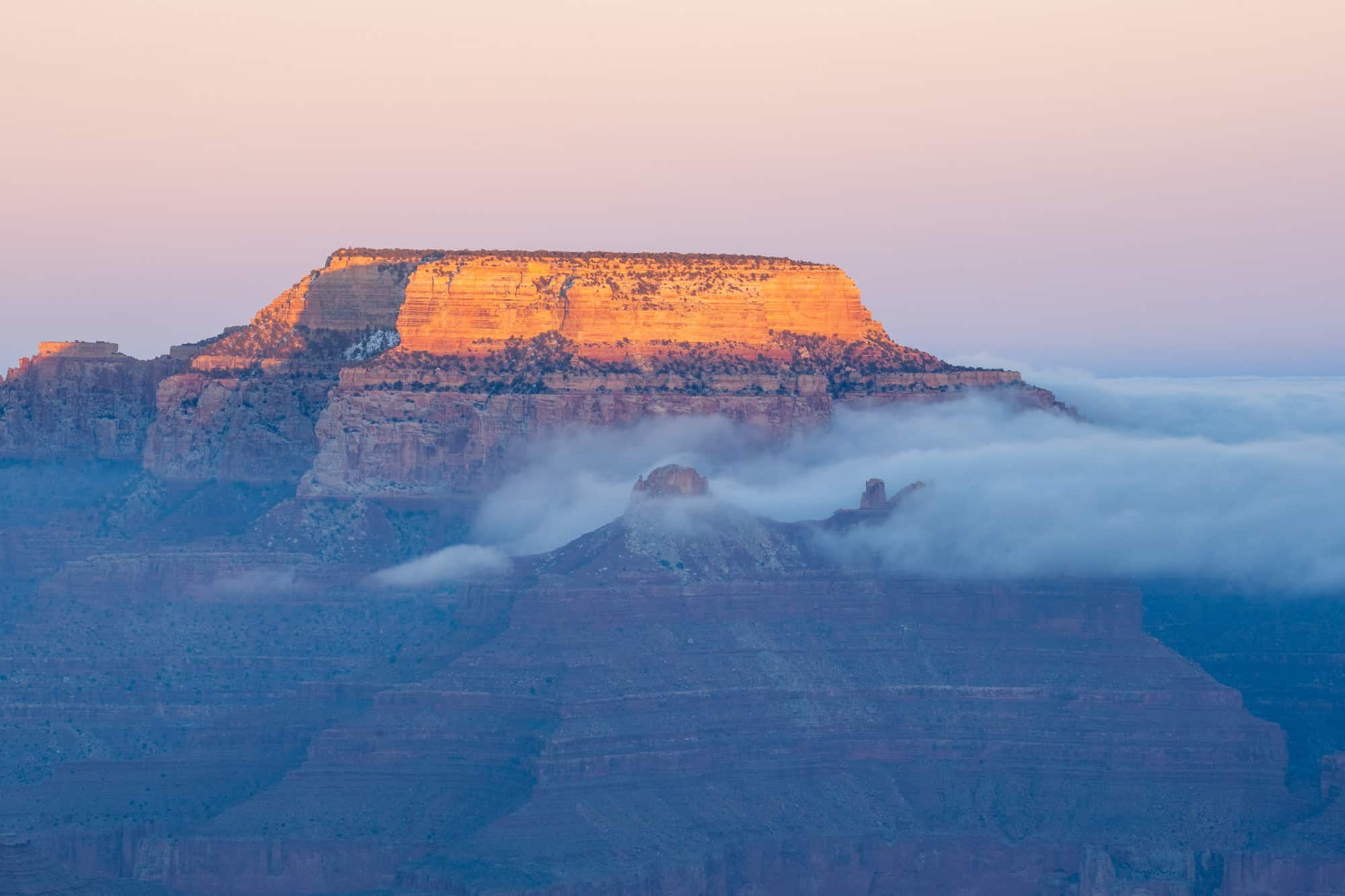 sunset at the south rim of the grand canyon, in this case one of the plateaus is shown with orange light and low hanging clouds