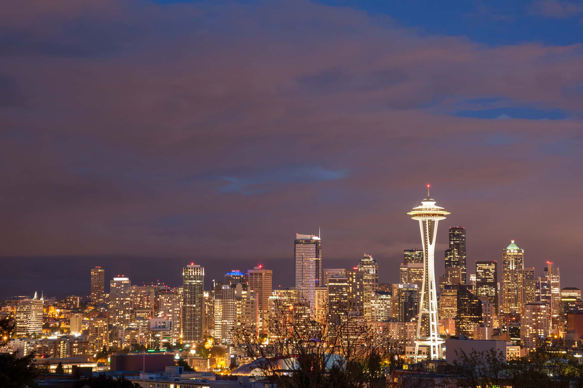 the seattle skyline with the buildings lit up at dusk before a purple sky