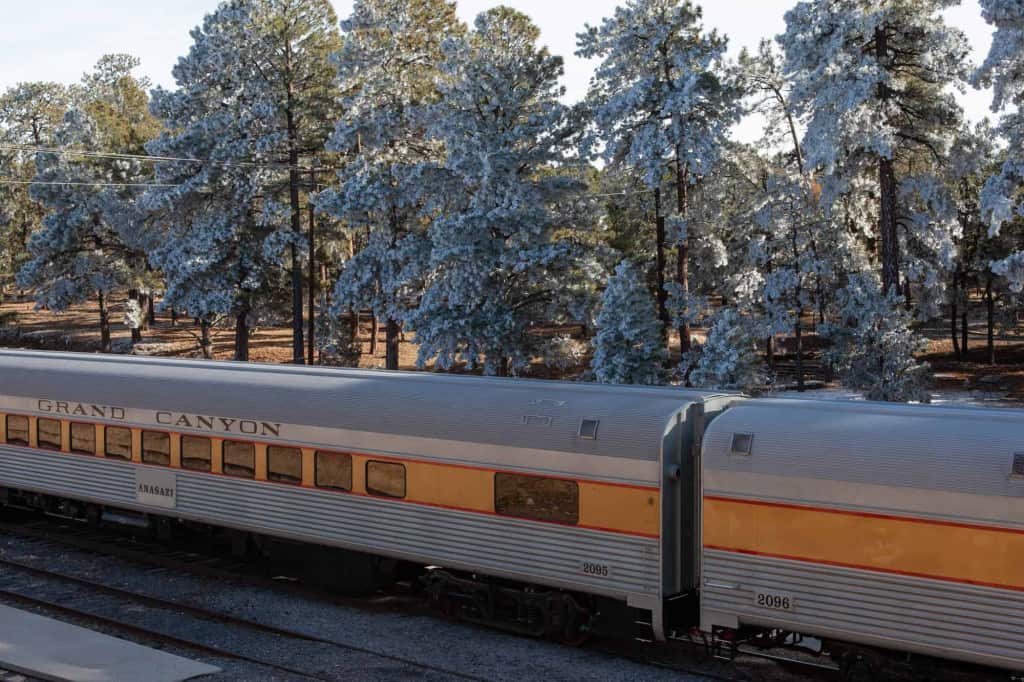 the grand canyon railway train sits on the tracks before snow covered trees