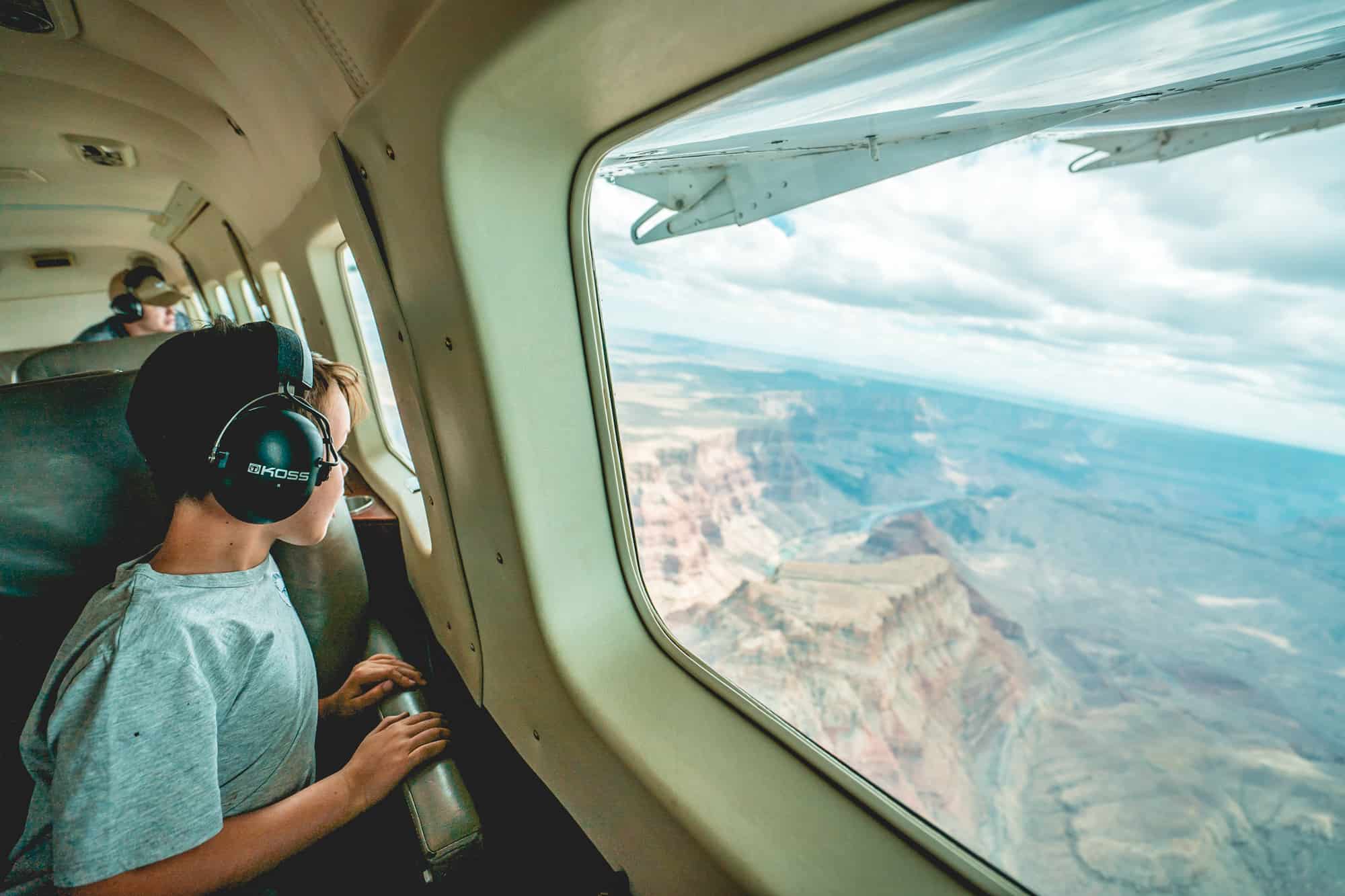 a young boy looks out the window at the grand canyon during a airplane flight over the canyon