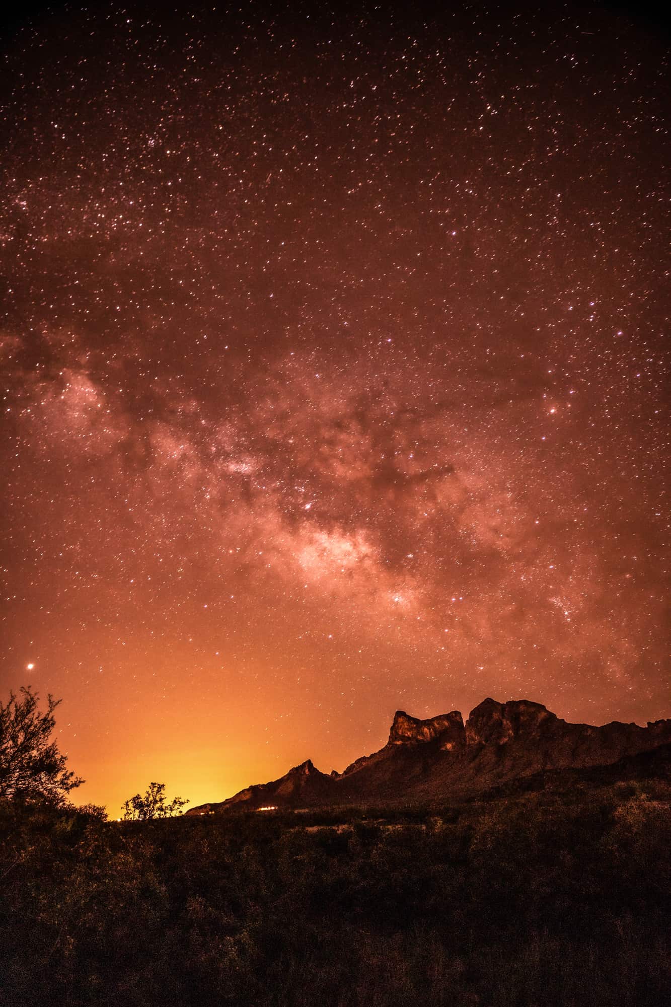 a night photo of picacho peak with the milky way in a reddish night sky