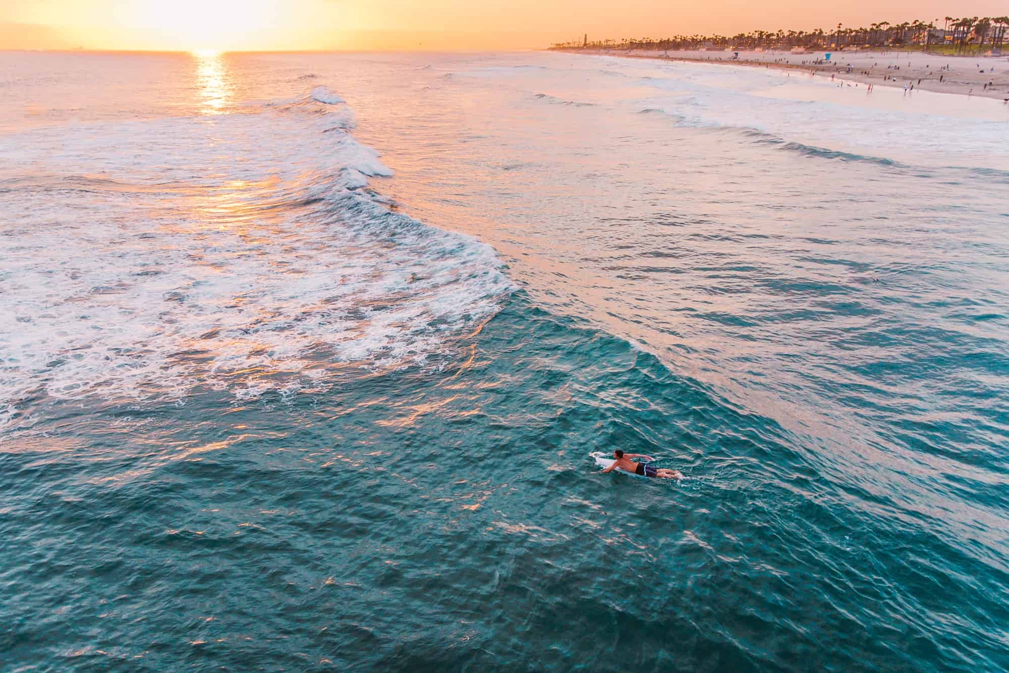 a surfer lays on his board paddling in the ocean waves at huntington beach