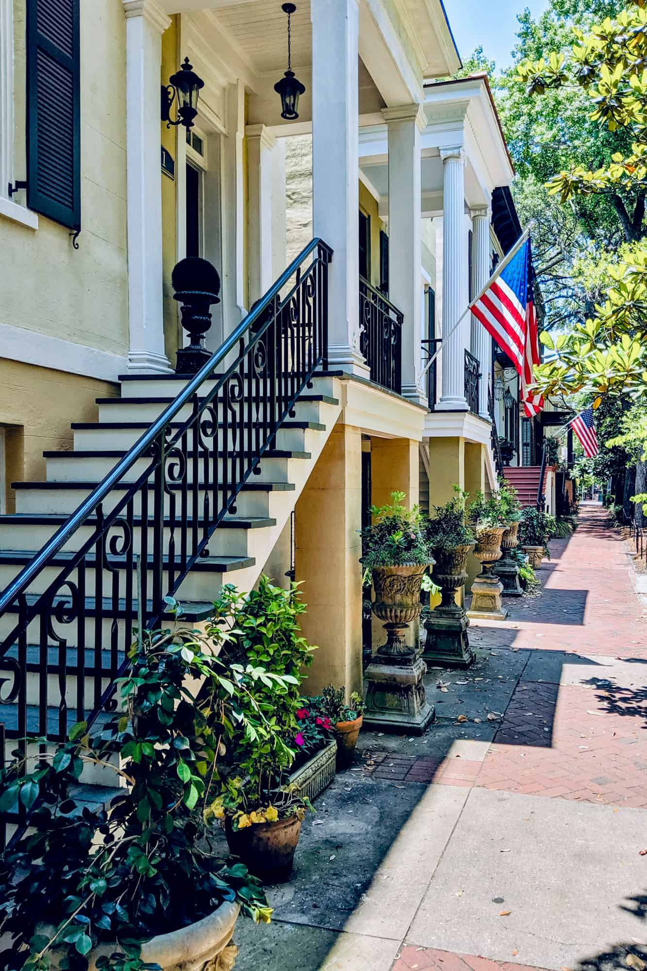 jones street in savannah, american flags hang outside historic homes along the tree lined sidewalk