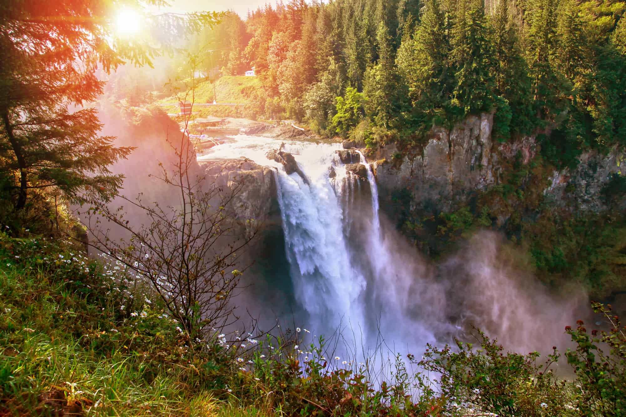 snoqualmie falls at sunset with sun shining on the op of the falls as it flows down over the cliff