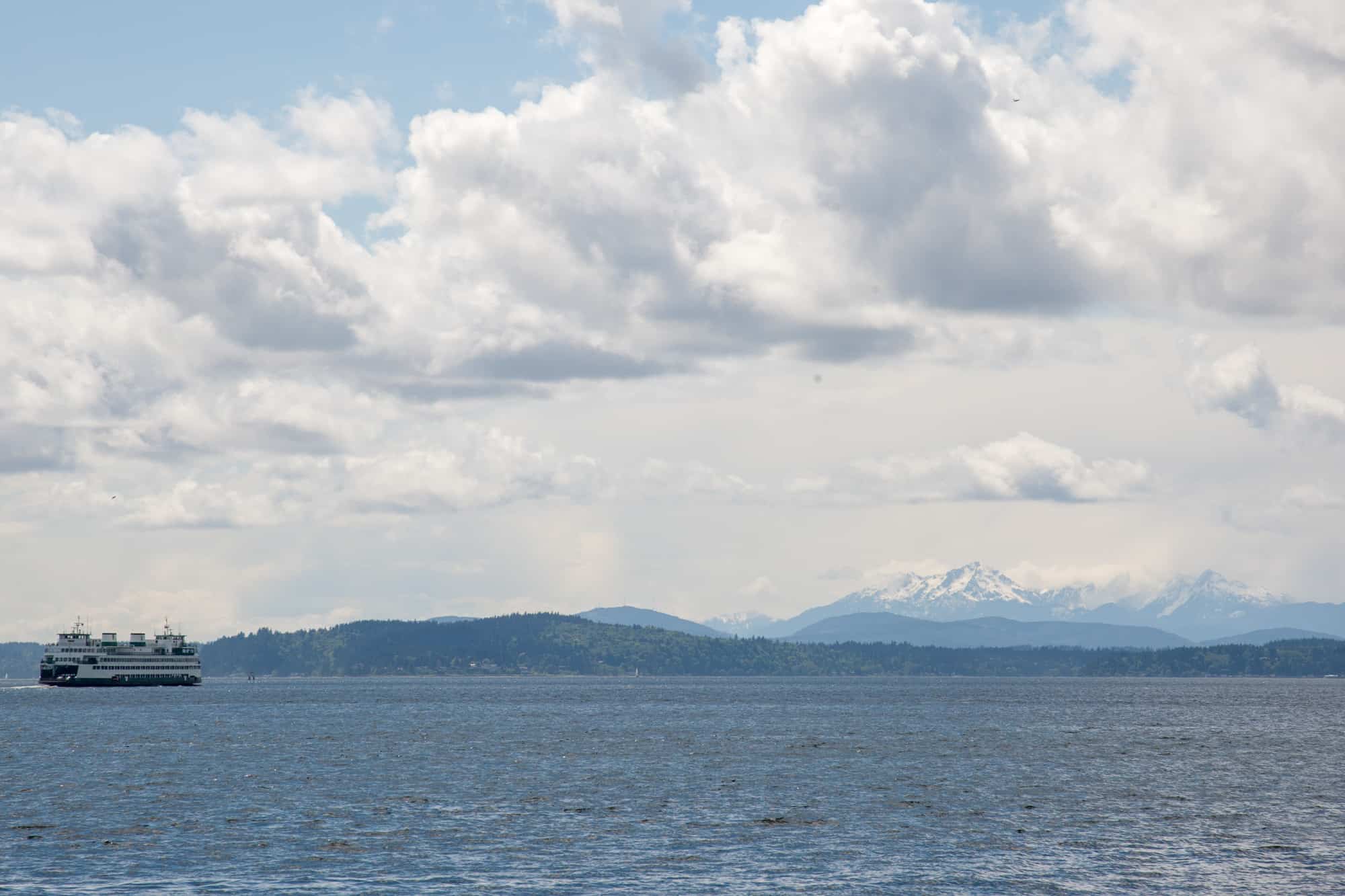 a ferry on the water in puget sound by seattle, in the distance you can see land and mountains