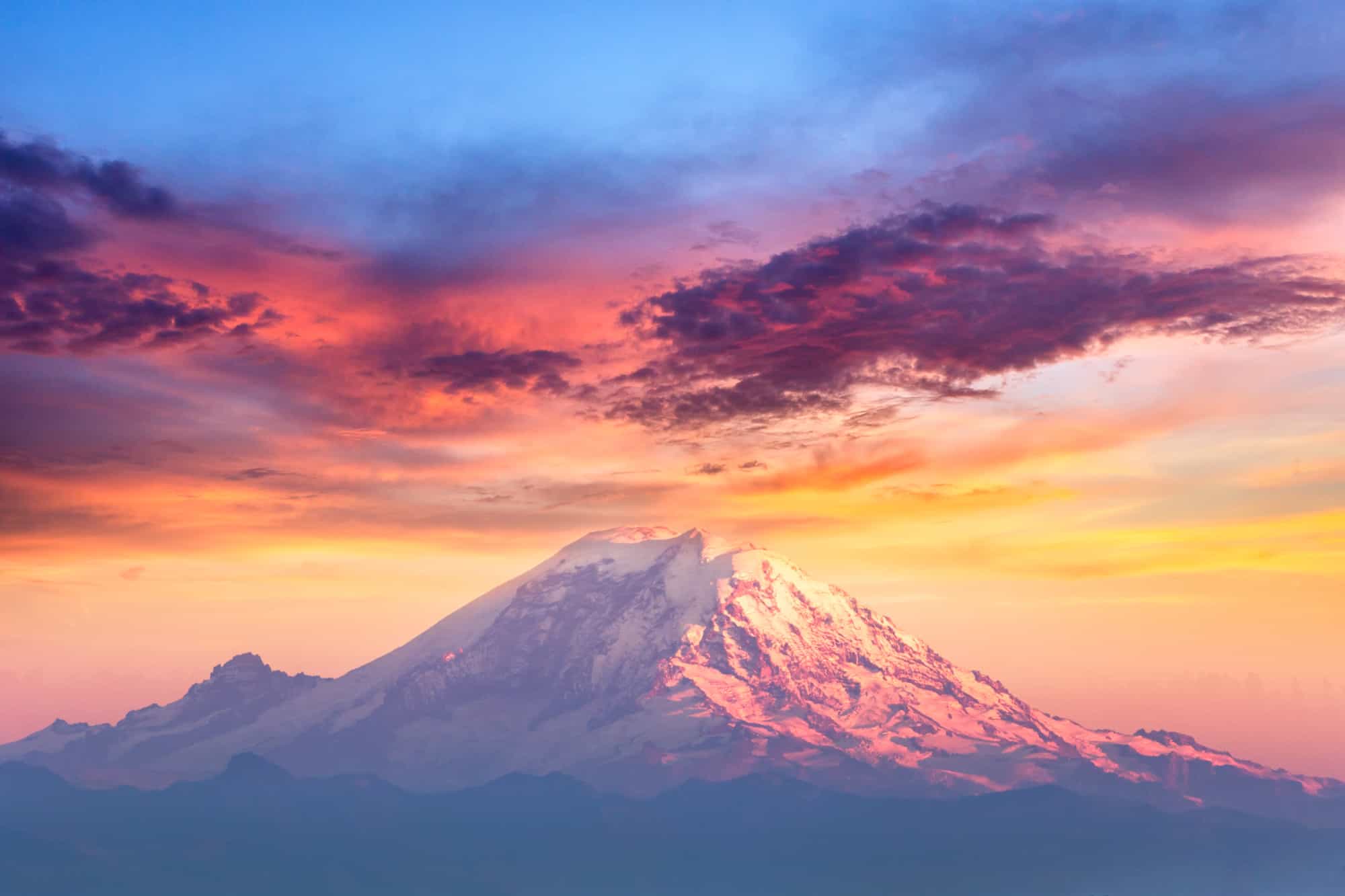 the top of mount rainier at sunset, with oranges, pinks and purples glowing above the snow covered peak