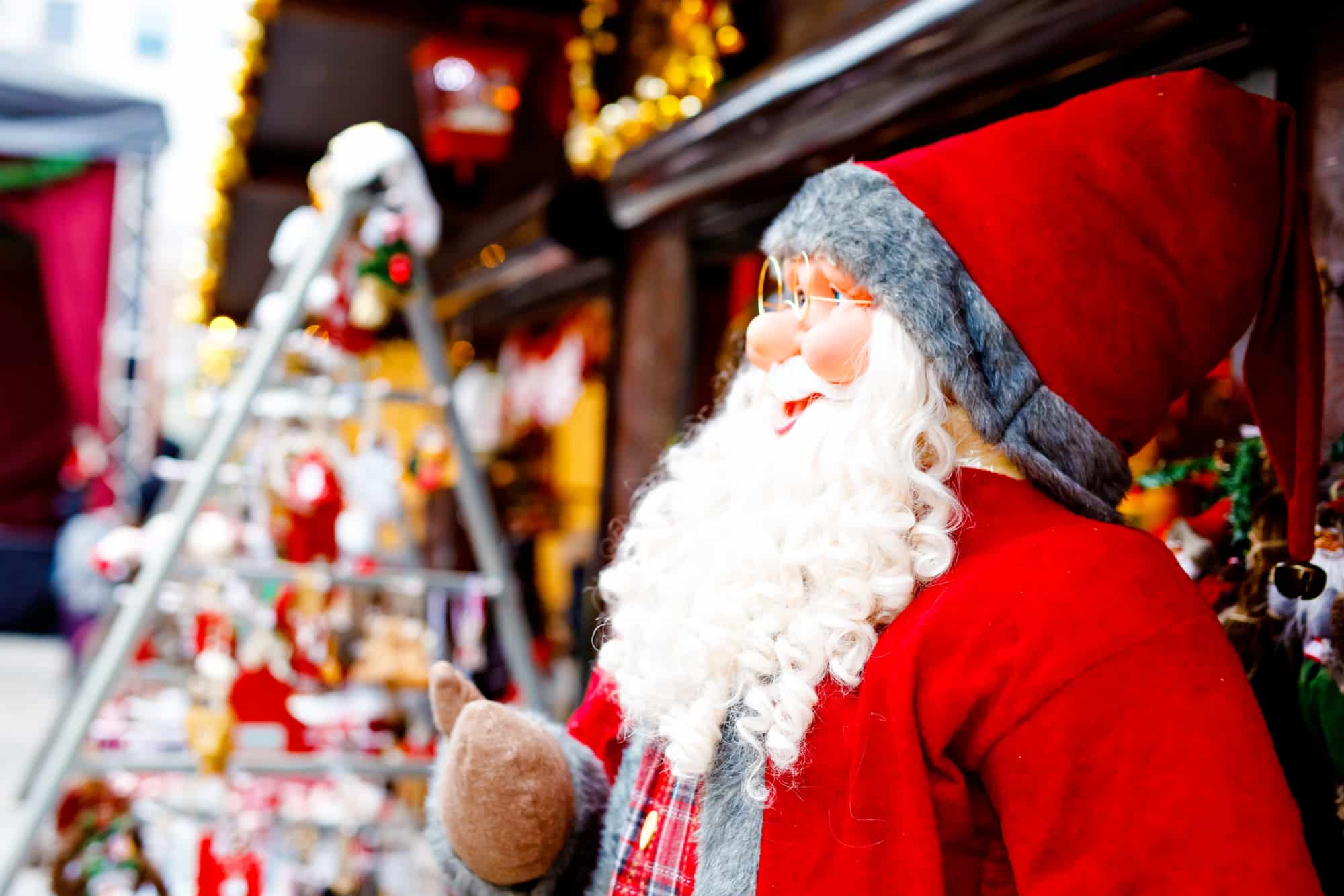 a santa sits at a christmas market with gifts on a shelf in the background