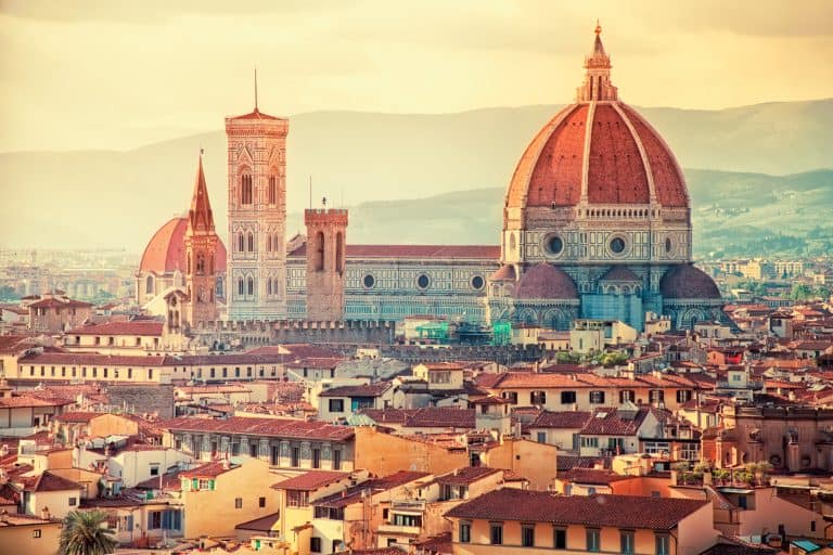 the florence cathedral stands tall above the city at sunset with yellows washing over the city