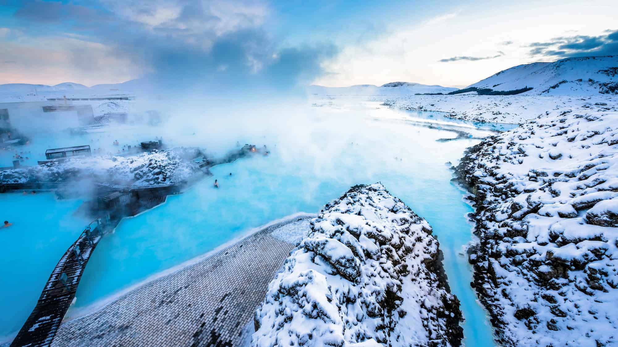 The steamy, milky blue waters of the Blue Lagoon geothermal spa, surrounded by snow-covered rocks and hills.