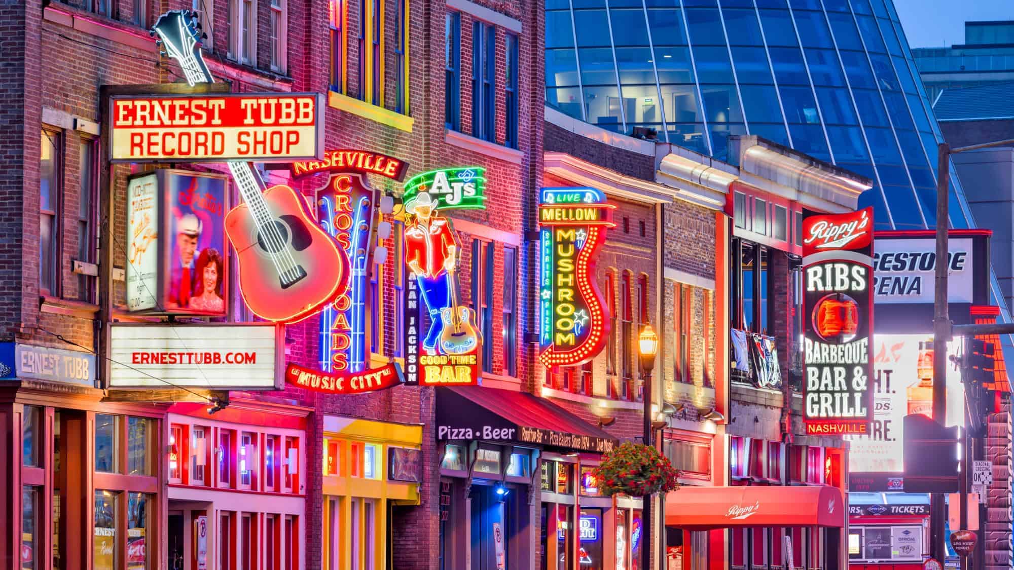 Neon signs on Broadway in Nashville at night, including Ernest Tubb Record Shop, Nashville Crossroads, and Rippy's Bar & Grill, illuminating the street with colorful lights