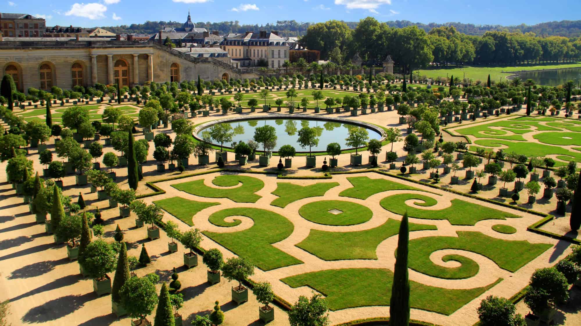 Manicured hedges and geometric patterns with a reflecting pool in the center, set against the backdrop of the grand palace buildings.