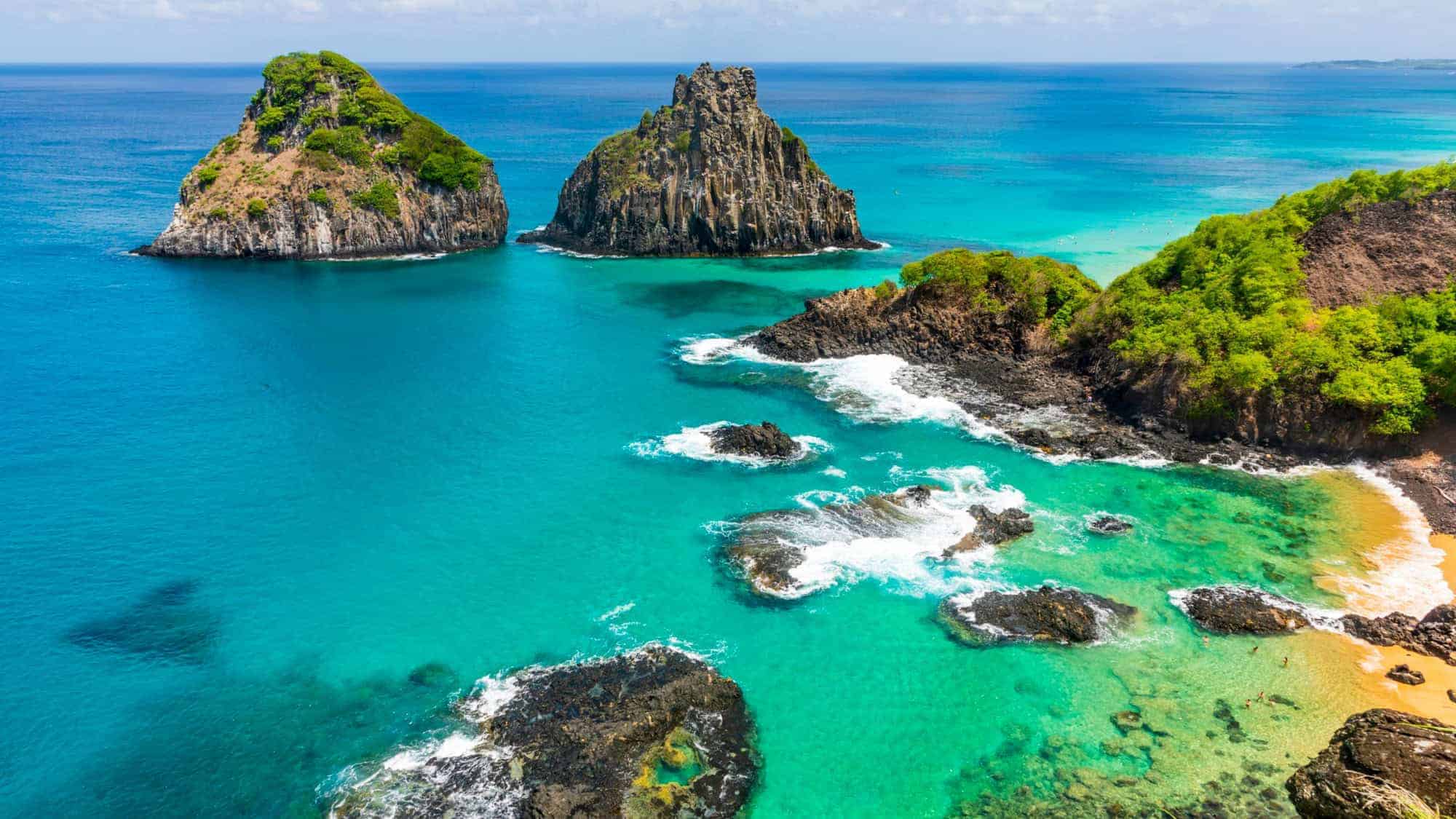 Aerial view of two rocky islands surrounded by clear turquoise waters and green foliage, part of the archipelago of Fernando de Noronha, Brazil.