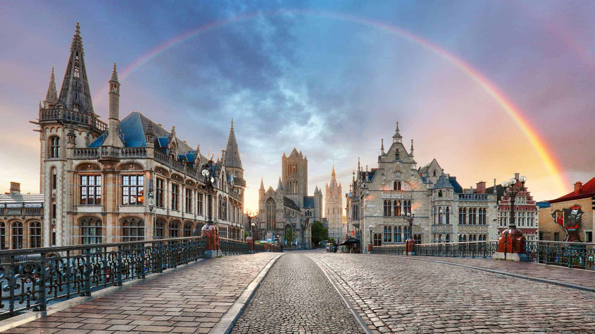 A stunning rainbow arches over the medieval architecture of Ghent, with its cobbled streets and historic buildings creating a picturesque scene.