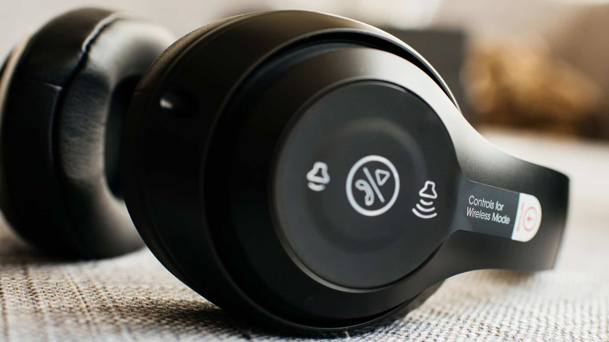 Close-up of black wireless headphones with control icons for playback and volume on the ear cup.