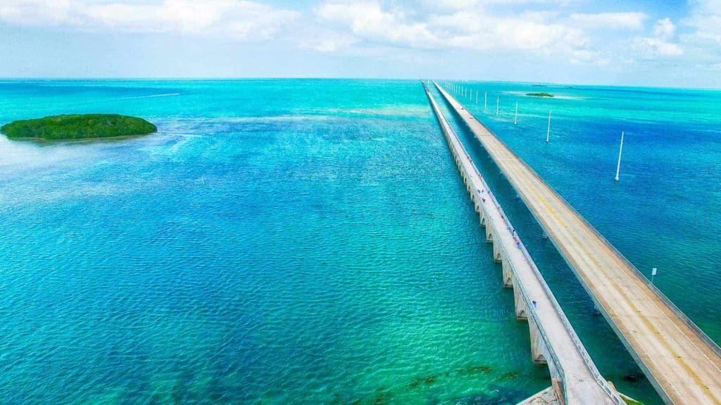 An expansive highway stretching over turquoise waters with a small green island in the distance.