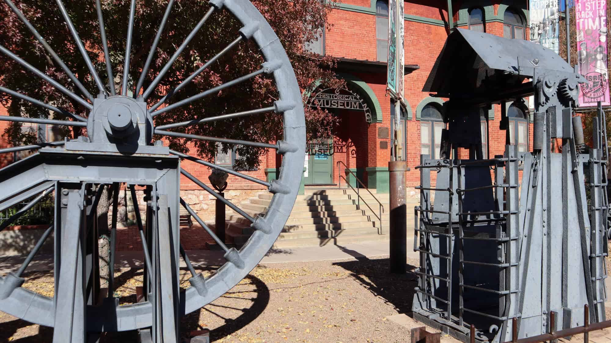 Industrial mining equipment is displayed outside a red brick historical museum, surrounded by autumn foliage.