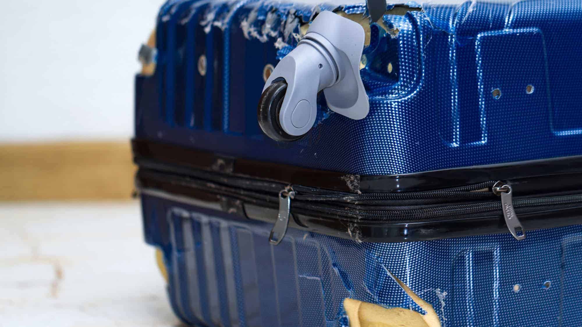 A close-up of a damaged blue suitcase with a broken wheel and torn edges.
