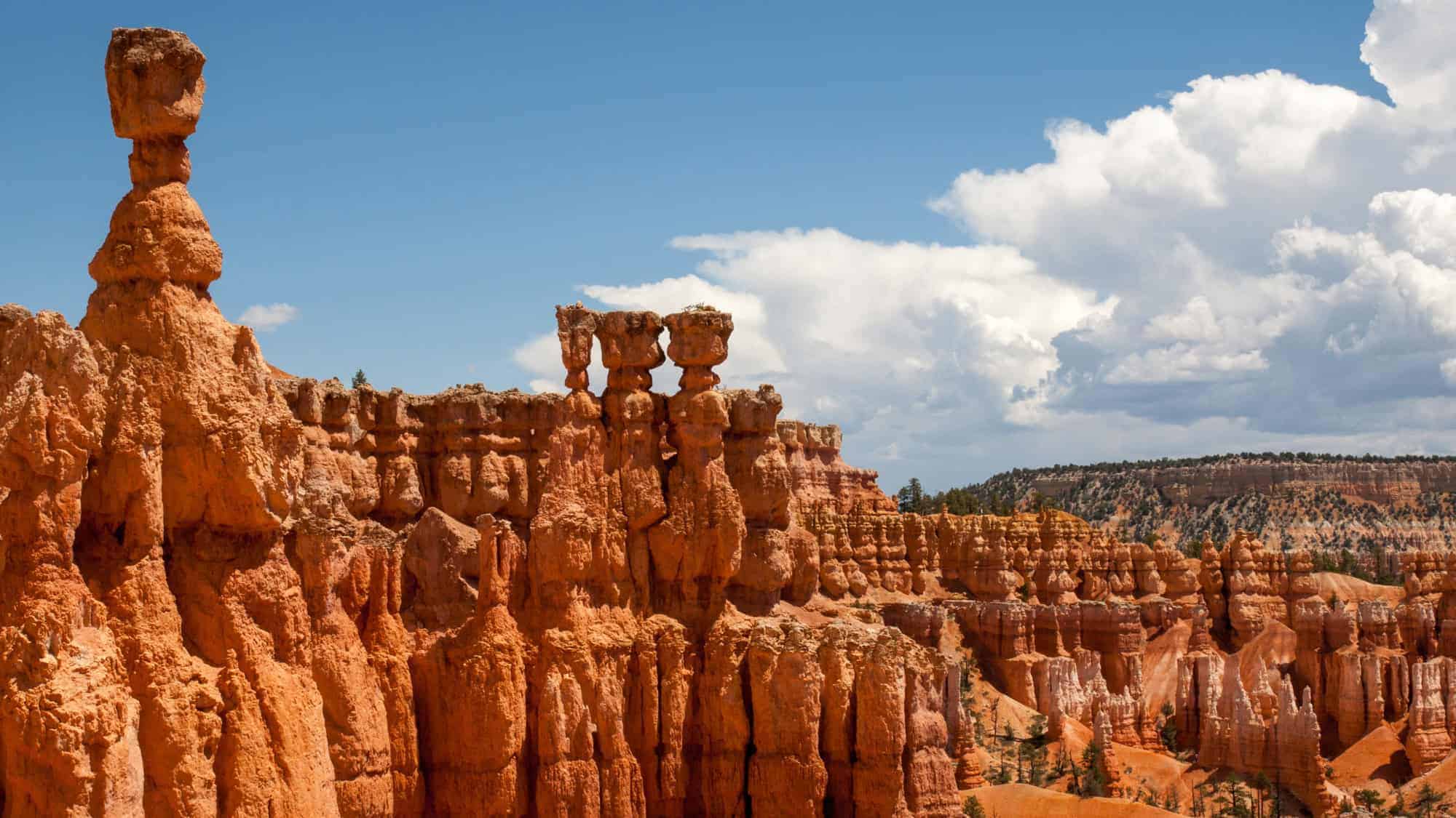 The unique, tall spires of red rock known as hoodoos, standing against a backdrop of blue sky and distant cliffs in Bryce Canyon National Park.