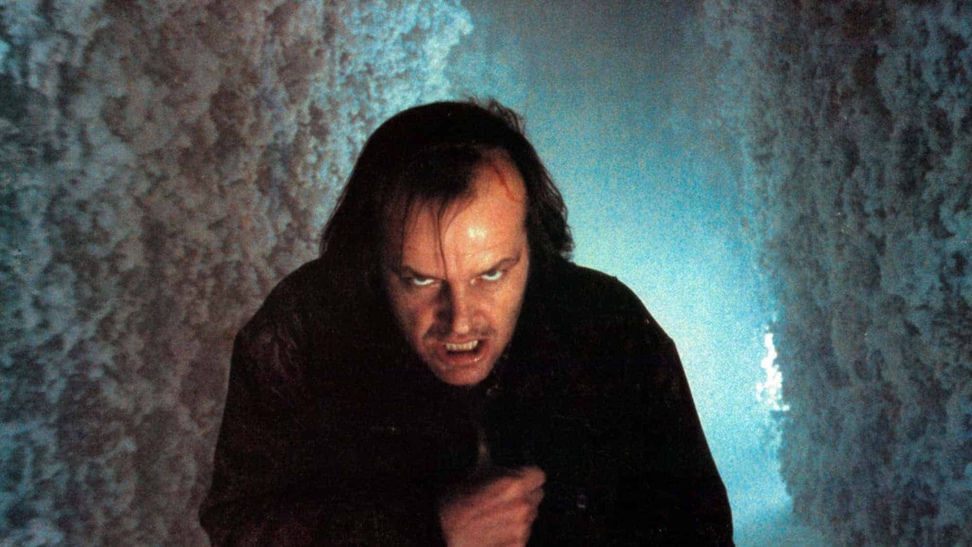 A man with a crazed expression, disheveled hair, and a menacing look is seen in a narrow, icy corridor. The lighting is eerie, casting a cold, foreboding atmosphere.