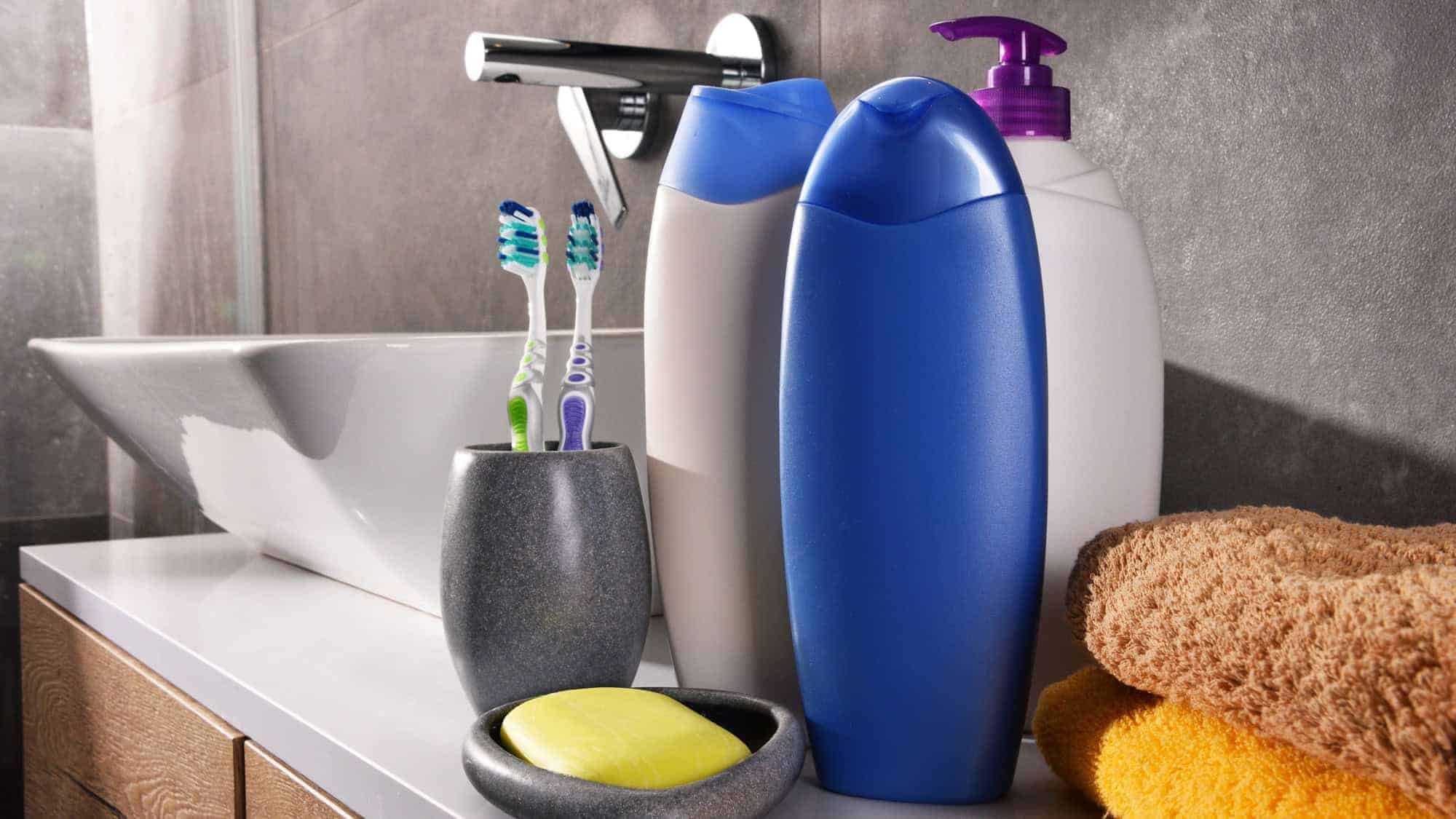 Toiletries arranged on a bathroom counter, including toothbrushes, soap, and bottles of lotion and shampoo next to a modern sink.