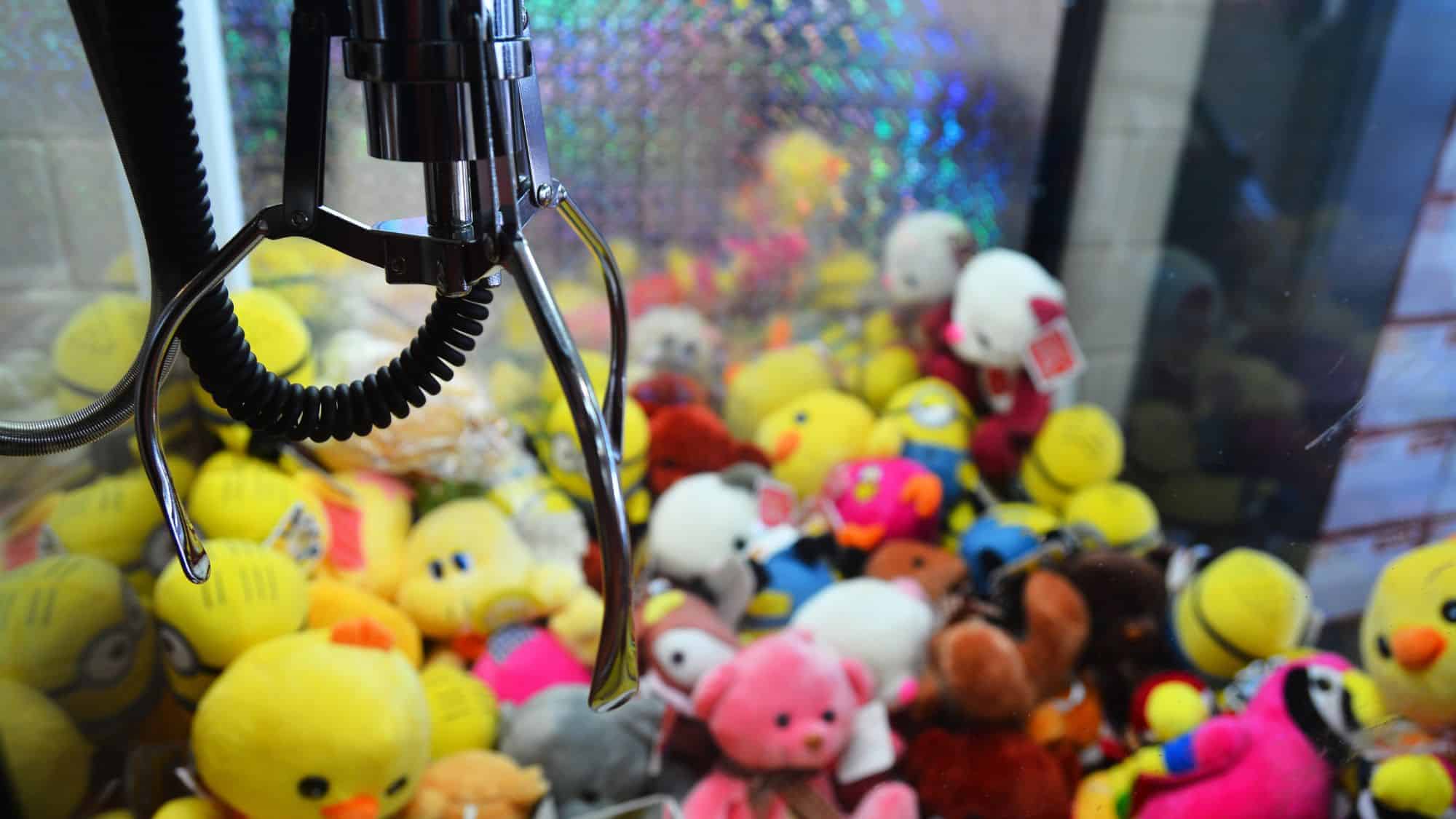 A close-up shot of a claw machine filled with various colorful stuffed toys, with the metallic claw hovering over the toys.