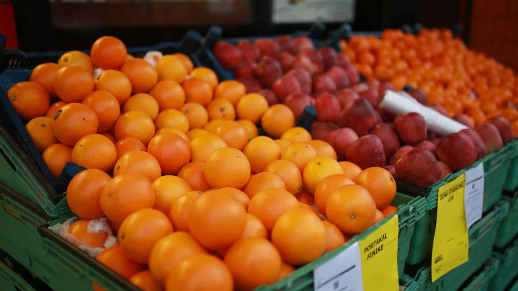 Fresh oranges and red apples are arranged neatly in crates at a market, with price tags visible nearby.