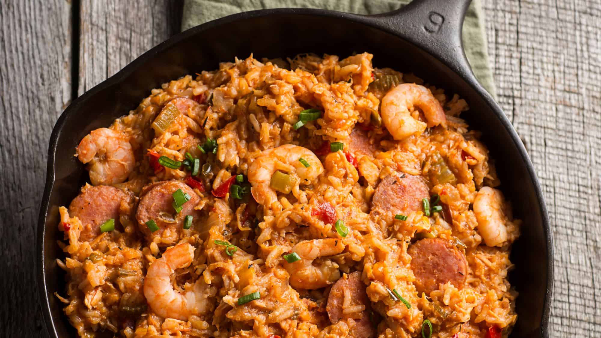 A skillet filled with a rich, hearty jambalaya dish, featuring shrimp, sausage, and rice with herbs.