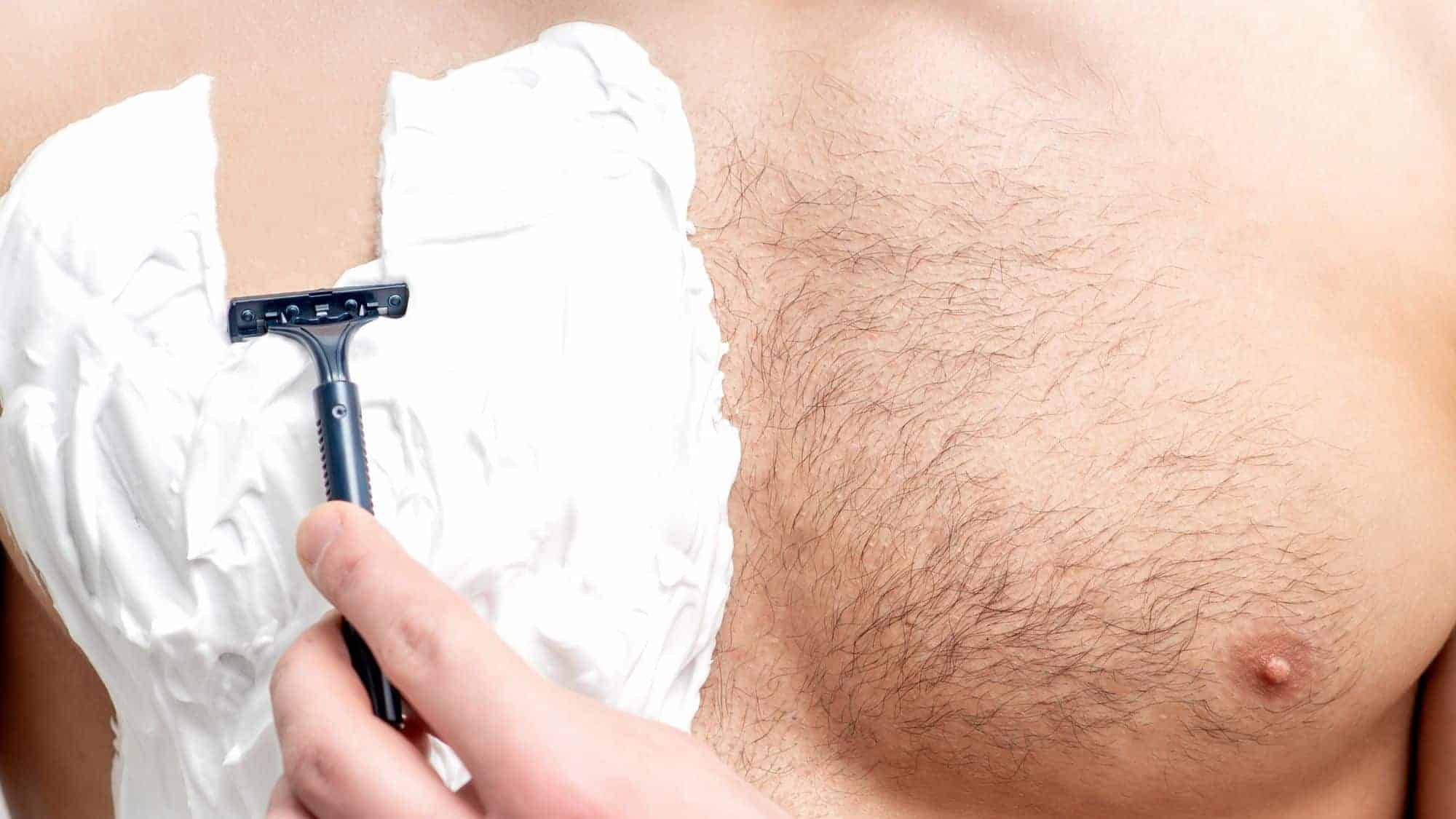 A person shaving their chest, half covered in shaving cream, using a razor on their bare skin.