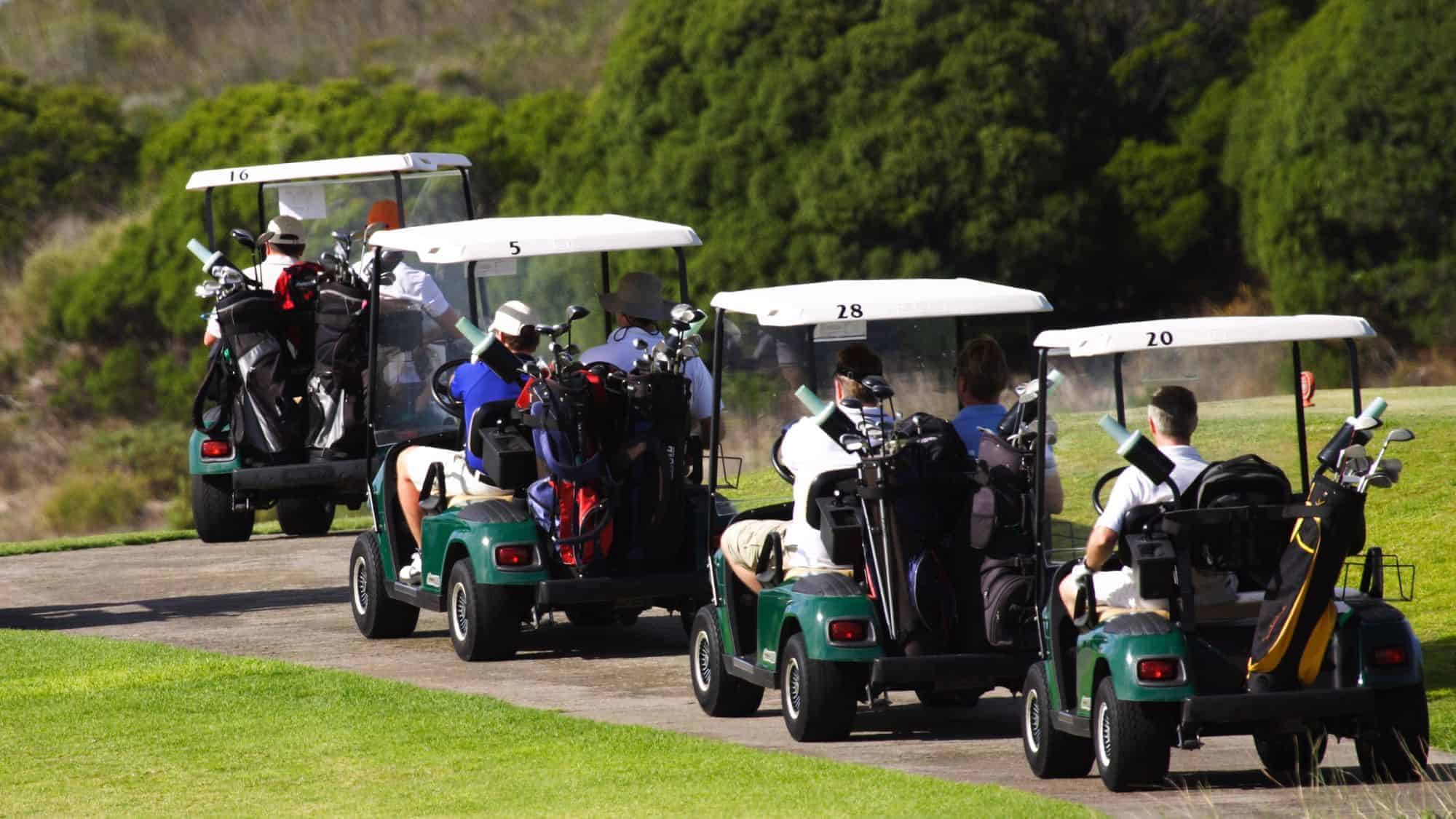 A row of golf carts filled with golfers driving on a path, surrounded by greenery.