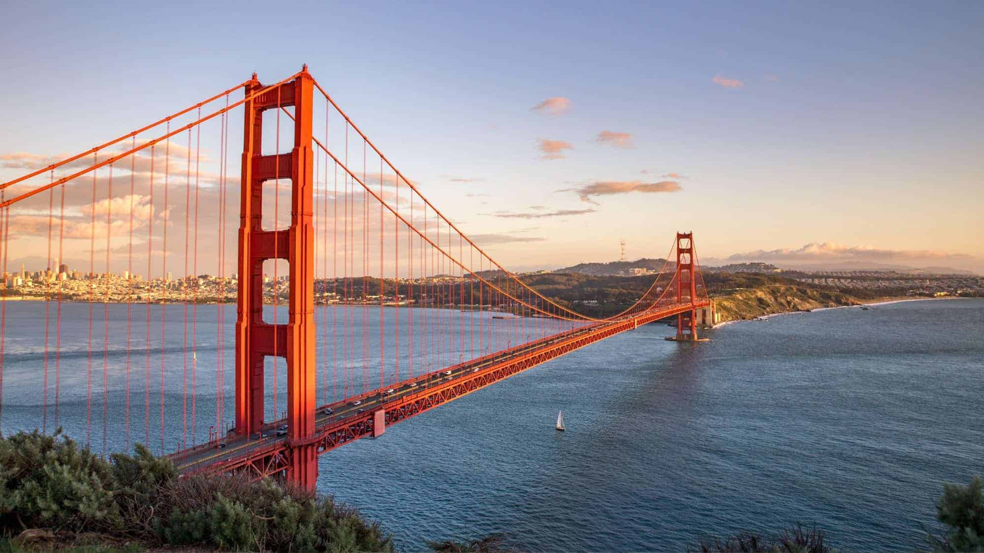 A scenic view of the iconic Golden Gate Bridge in San Francisco at sunset, with its red towers and cables silhouetted against the sky and water.