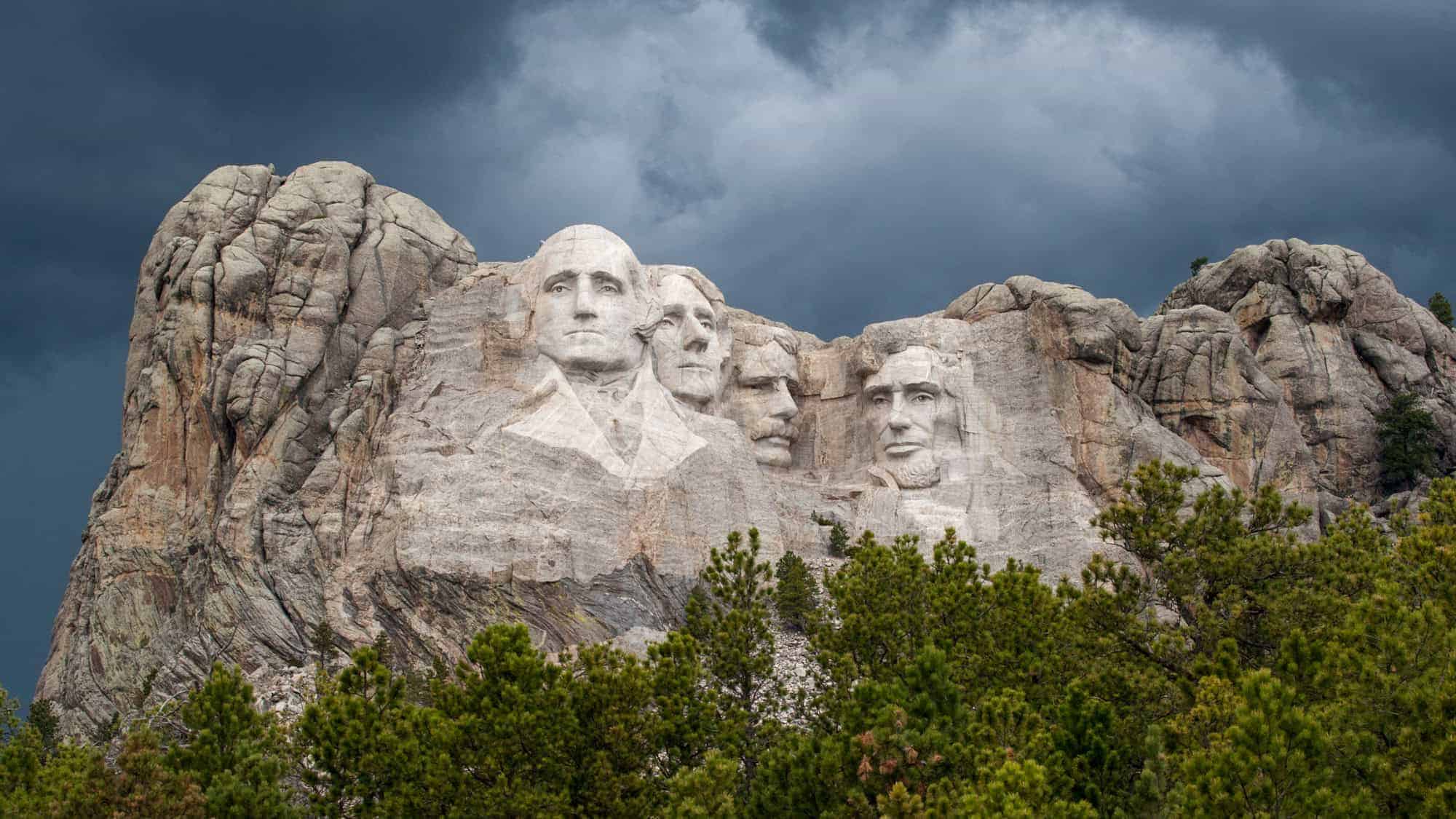 The famous Mount Rushmore National Memorial featuring the carved faces of U.S. Presidents George Washington, Thomas Jefferson, Theodore Roosevelt, and Abraham Lincoln, set against a stormy sky.