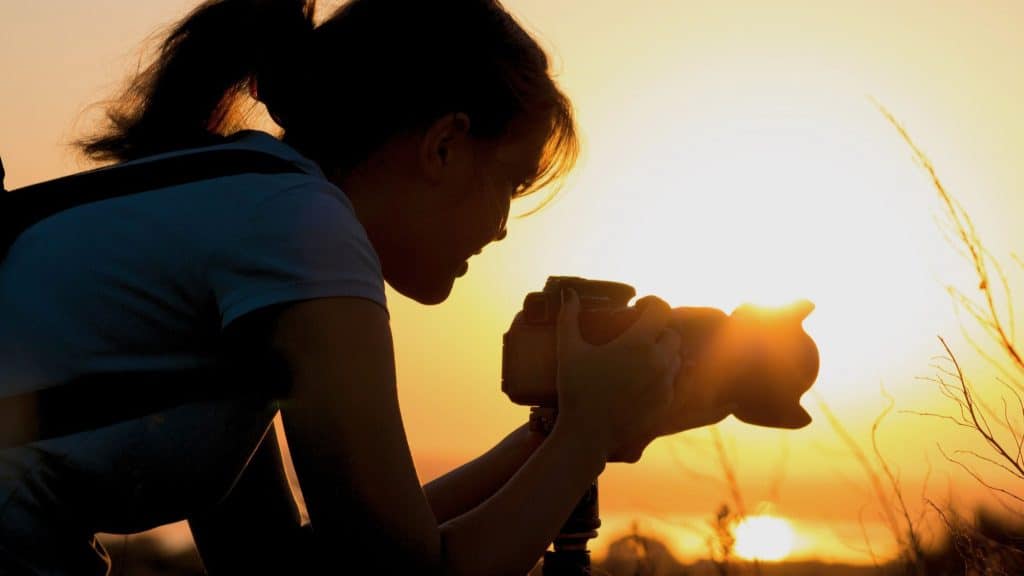 A silhouette of a photographer capturing the sunset with a camera on a tripod, set against a golden-orange sky during the golden hour.