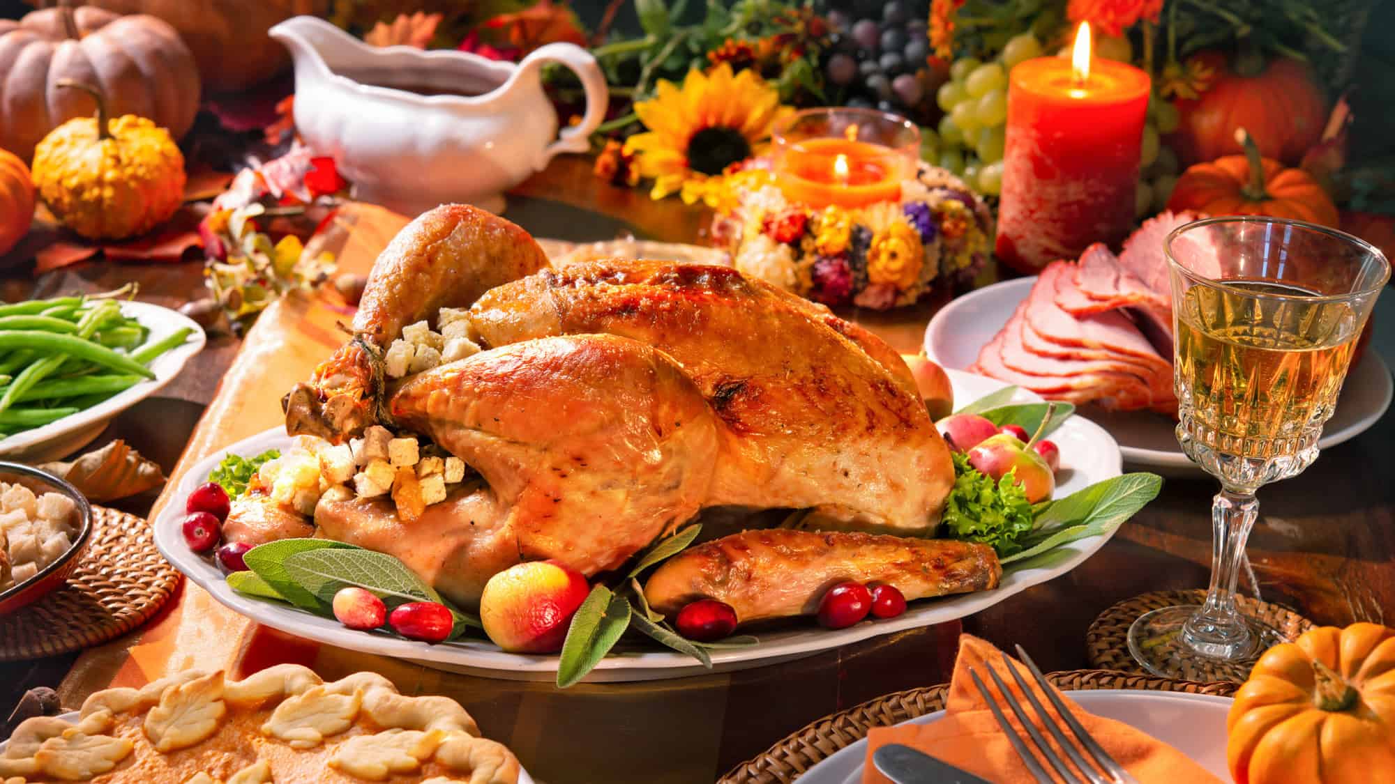 A golden roasted turkey stuffed with bread cubes is surrounded by cranberries, fresh herbs, and autumn-themed side dishes on a festive table.