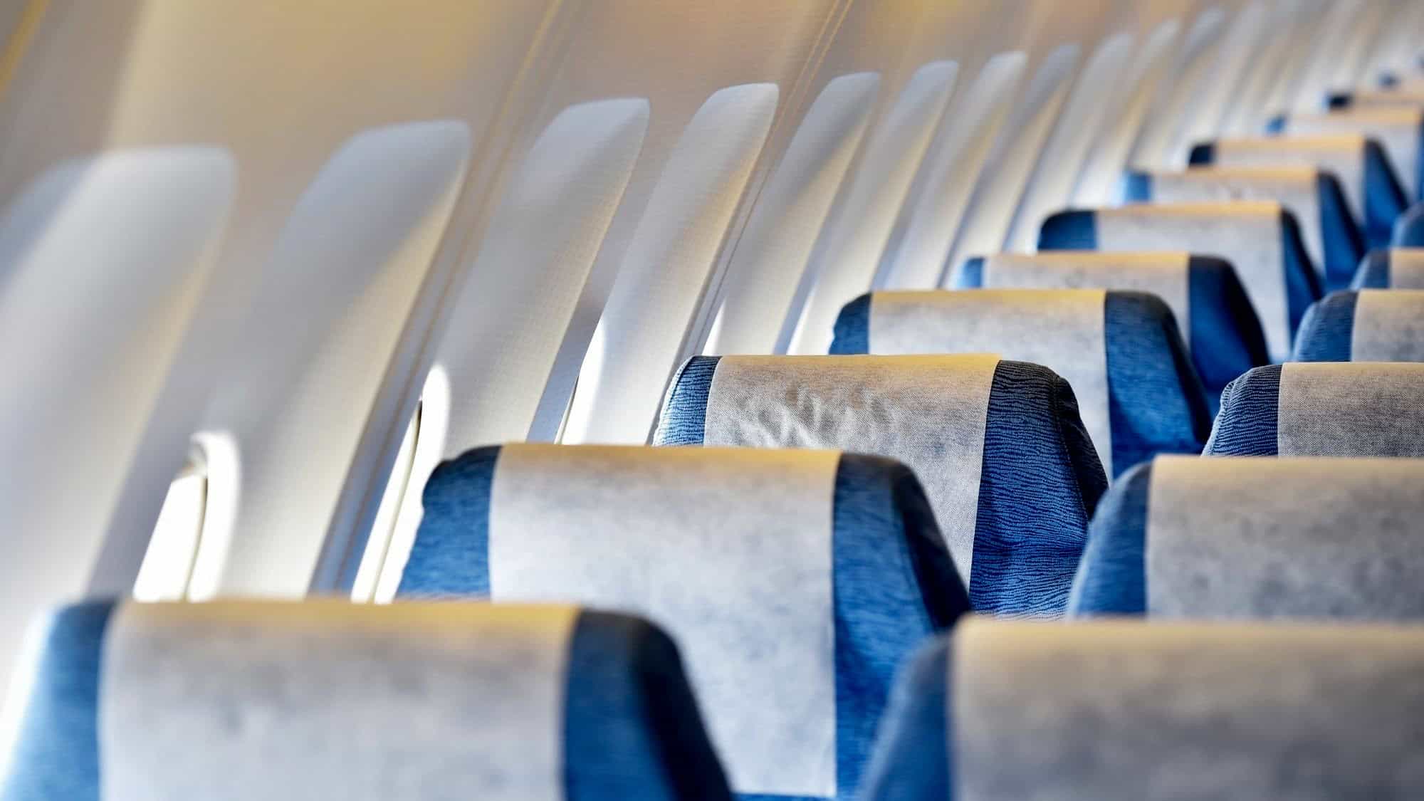 Blue fabric airline seats with white headrest covers line the cabin beneath sunlit windows.