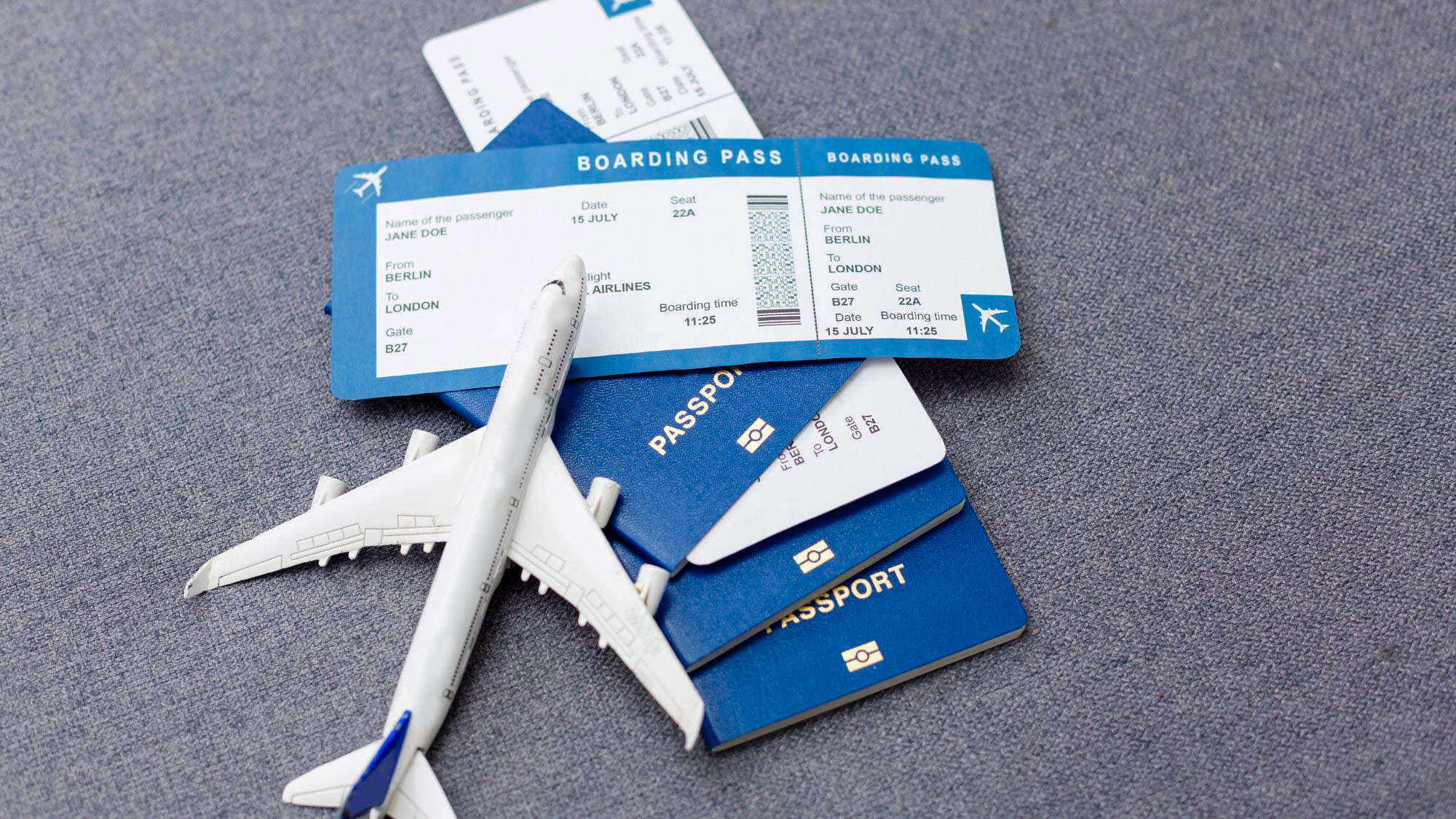 A close-up of blue passports, a model airplane, and a boarding pass from Berlin to London laid out on a gray surface.
