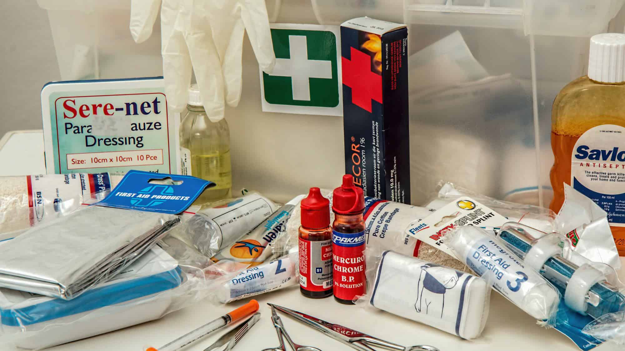 An assortment of medical supplies including bandages, antiseptic, scissors, gloves, and ointments spread across a surface.