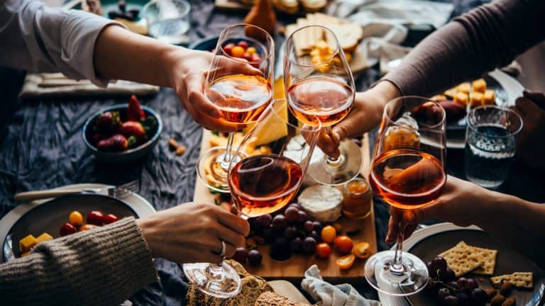 A group of friends clinks their wine glasses together over a table full of charcuterie, fruits, and snacks, creating a celebratory toast.