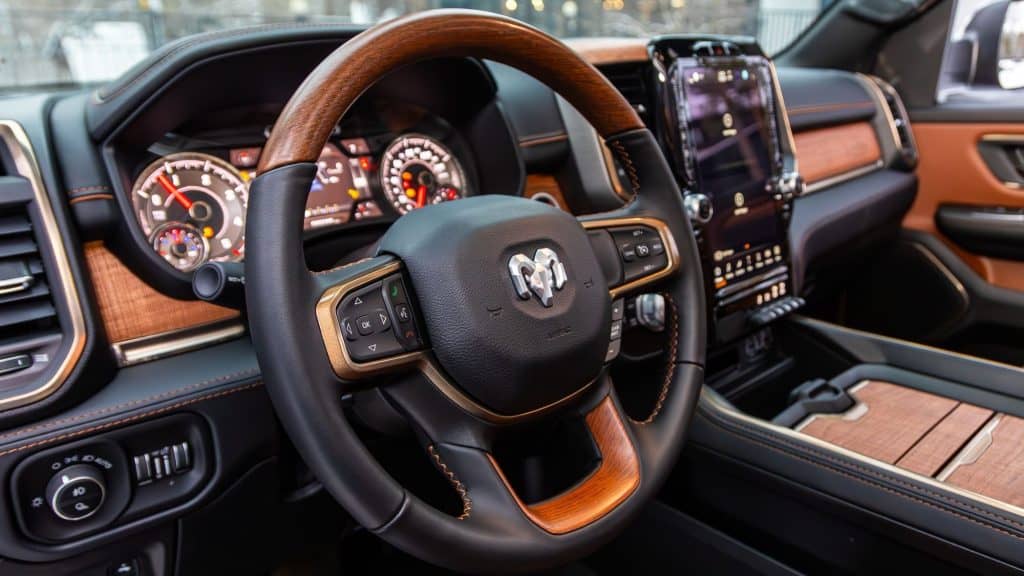 A detailed view of the luxurious interior of a Ram 1500 truck, featuring a leather-wrapped steering wheel with wood accents and a high-tech dashboard.