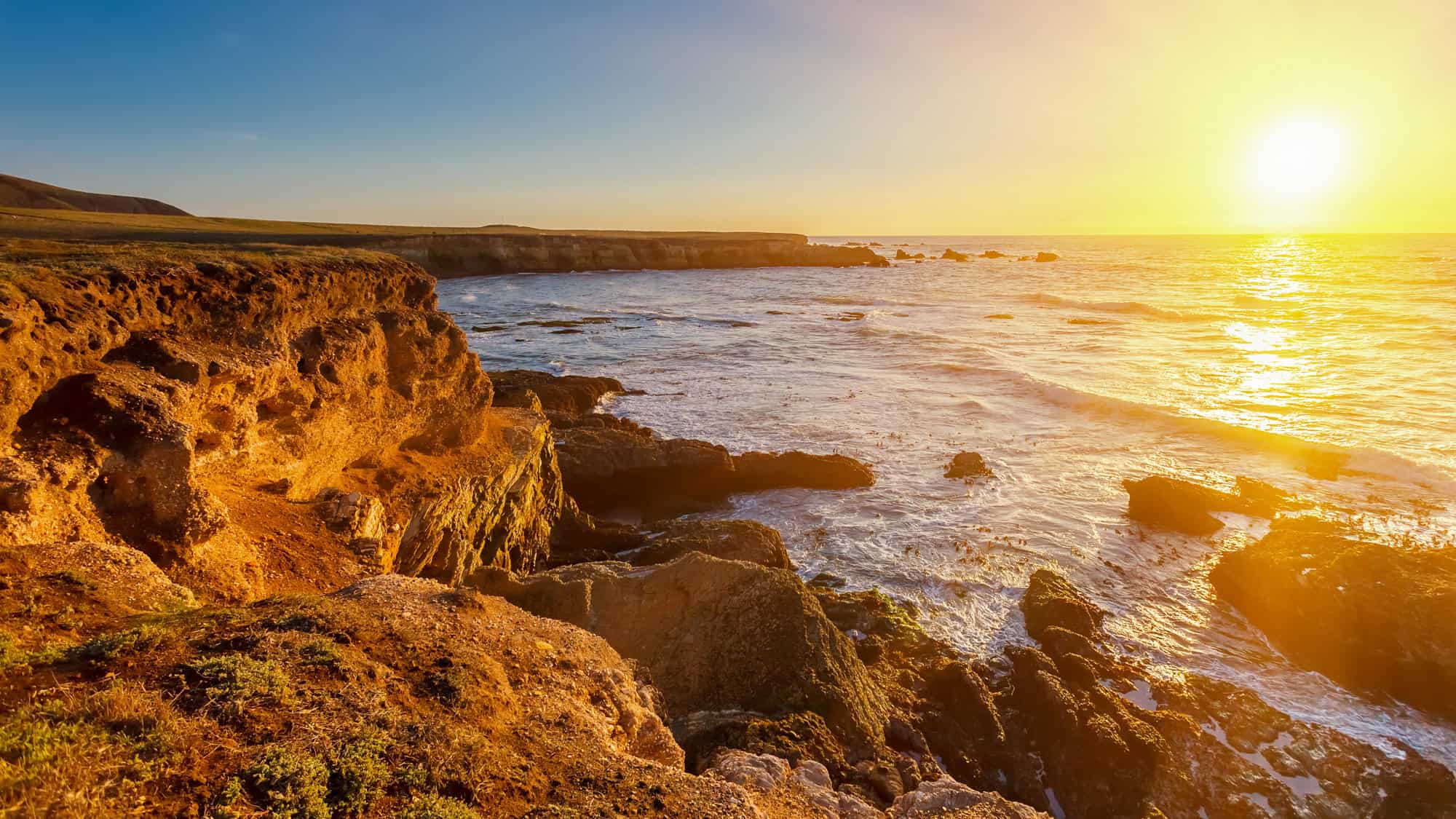 Golden sunlight illuminates rugged sea cliffs and waves along California’s dramatic coastline.