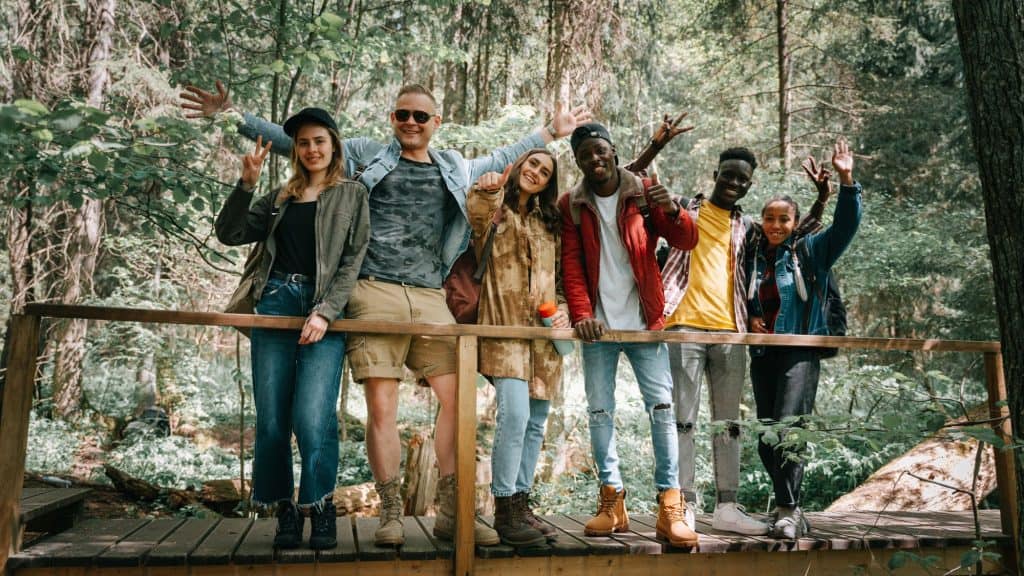 A group of adults stand on a wooden bridge in the woods.