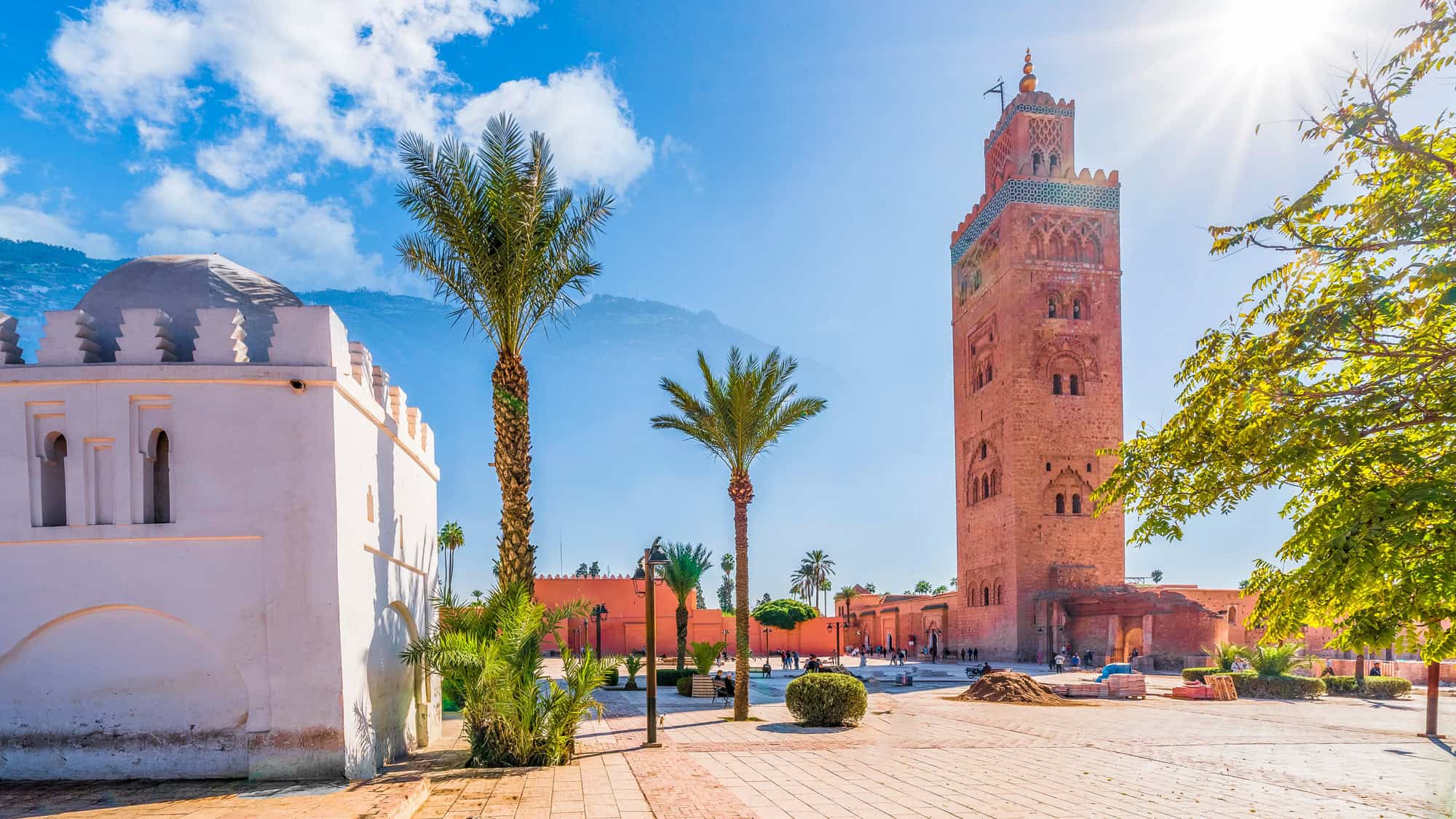 The sun shines over the towering minaret of the Koutoubia Mosque, surrounded by palm trees in Marrakech, Morocco.