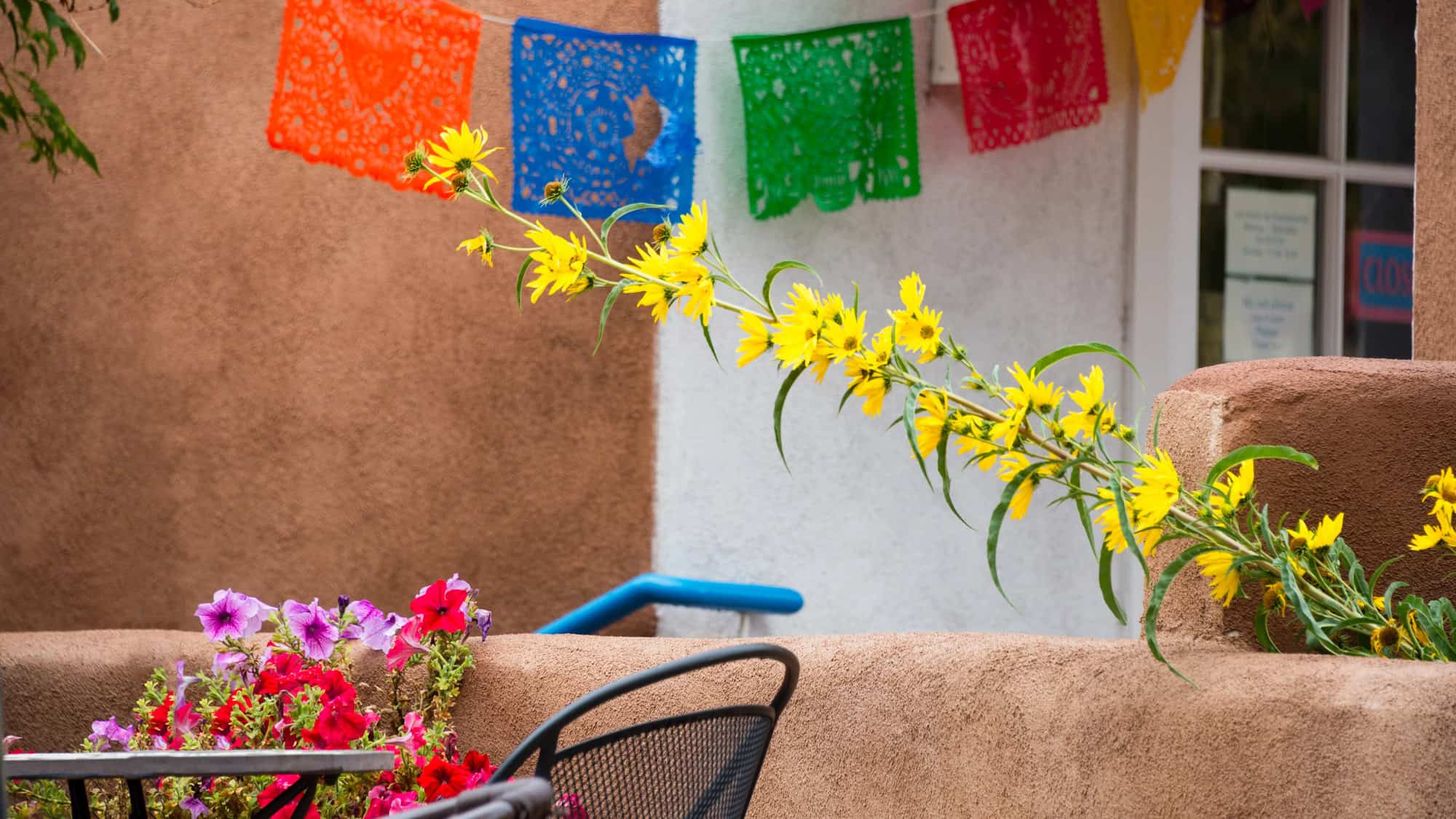 Bright yellow sunflowers and colorful papel picado banners decorate a rustic adobe courtyard.