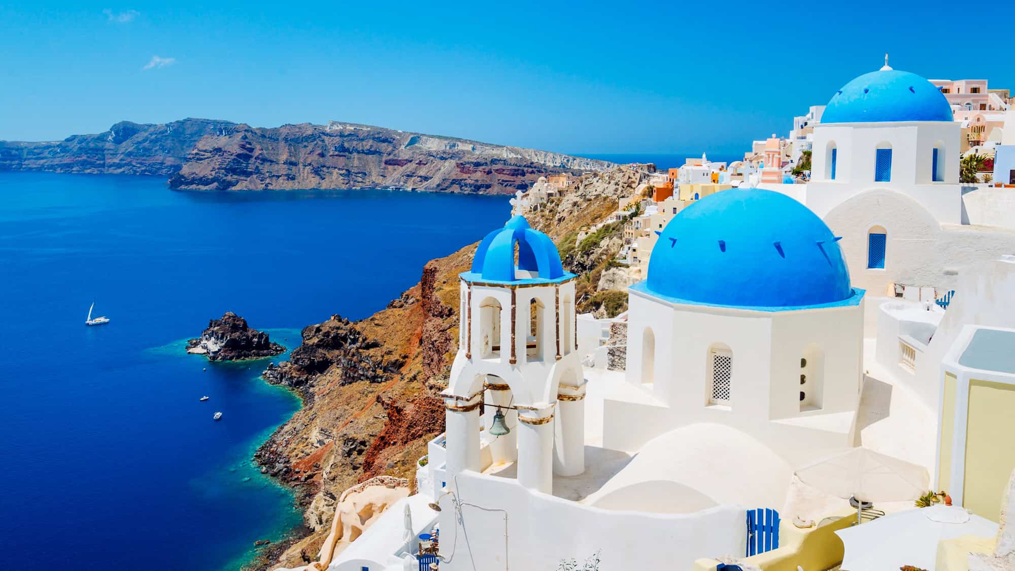 Whitewashed buildings with blue-domed roofs overlook the deep blue Aegean Sea in Santorini, Greece.