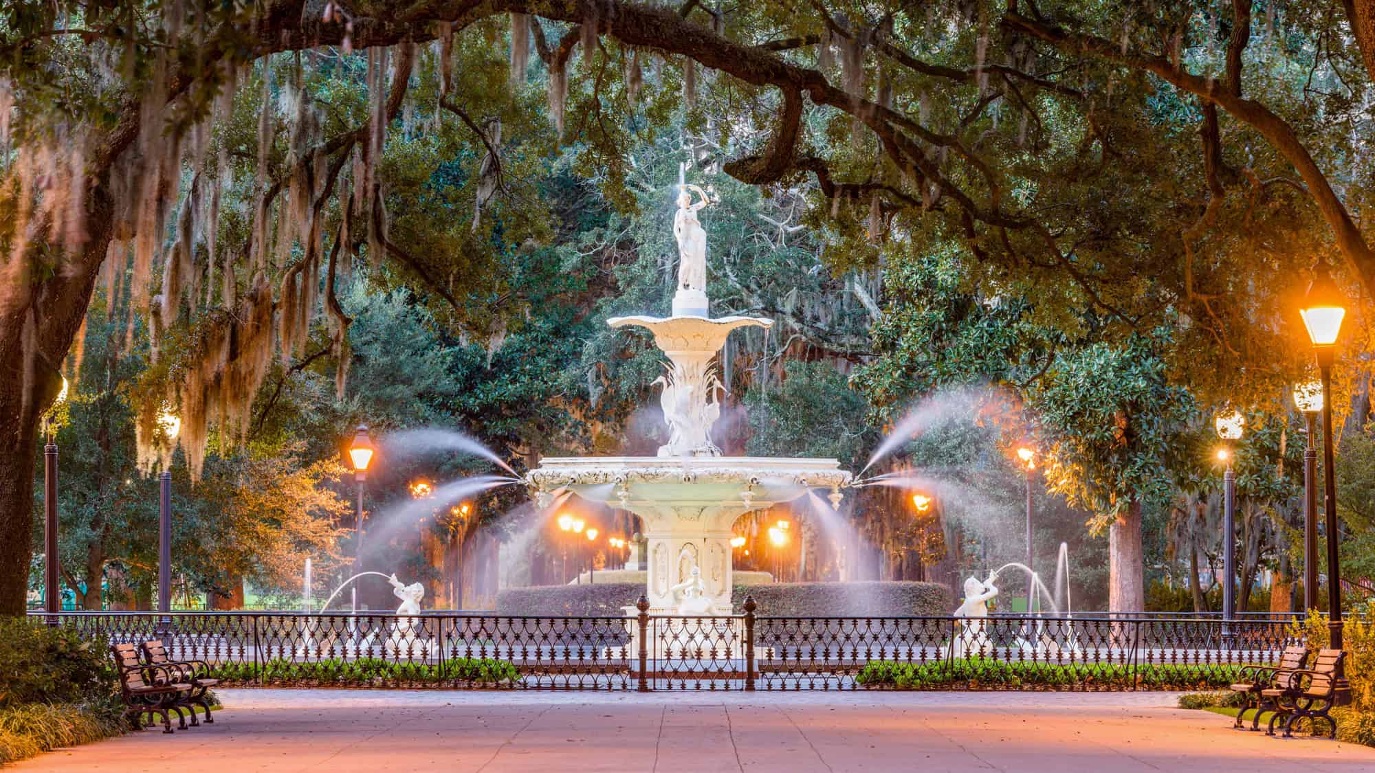 A grand white fountain sprays water beneath moss-draped oak trees in Savannah’s Forsyth Park.