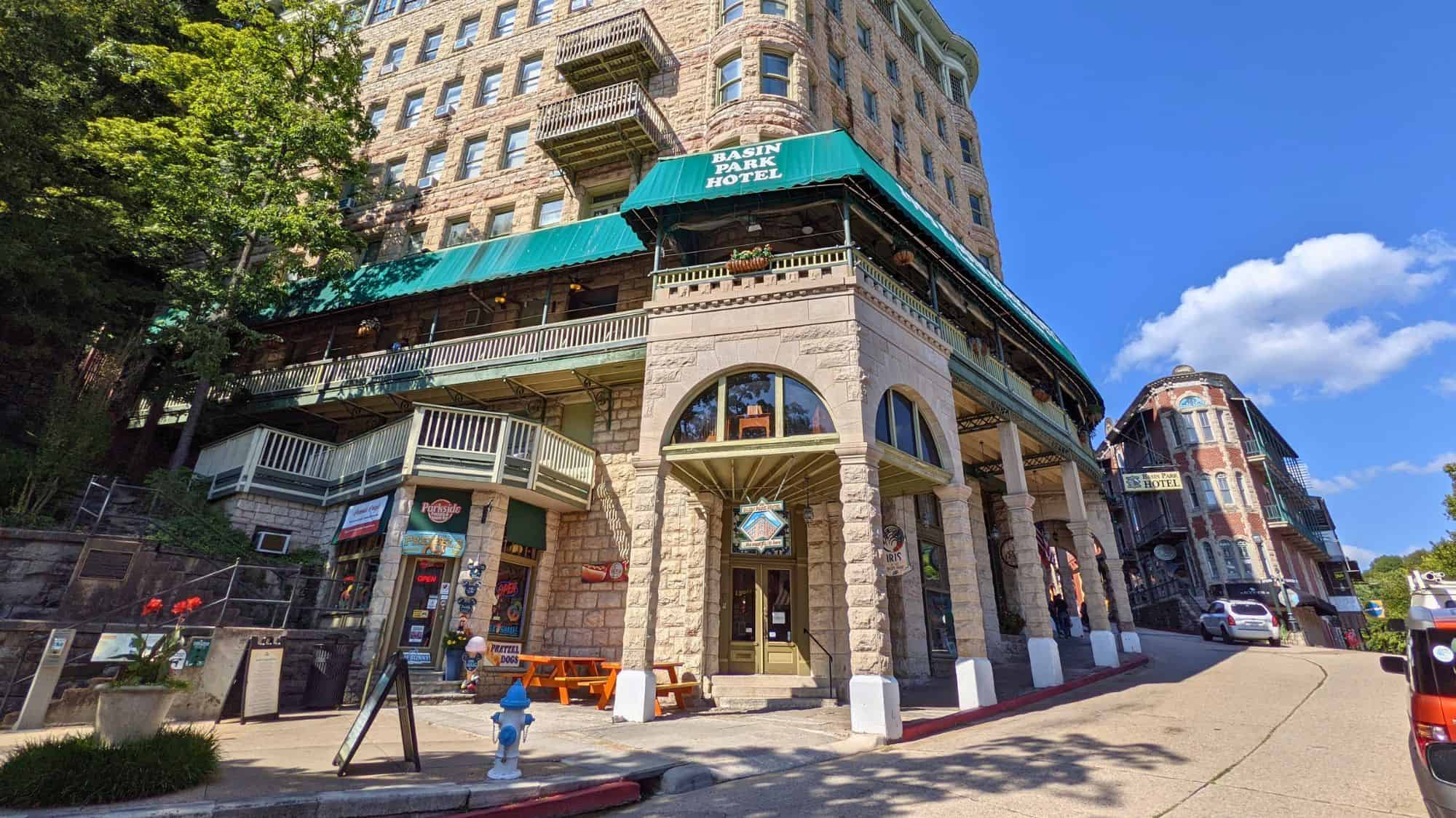 A historic stone hotel with green awnings perched on a hillside in Eureka Springs. The unique multi-level structure blends into the natural surroundings, with balconies overlooking the charming town.