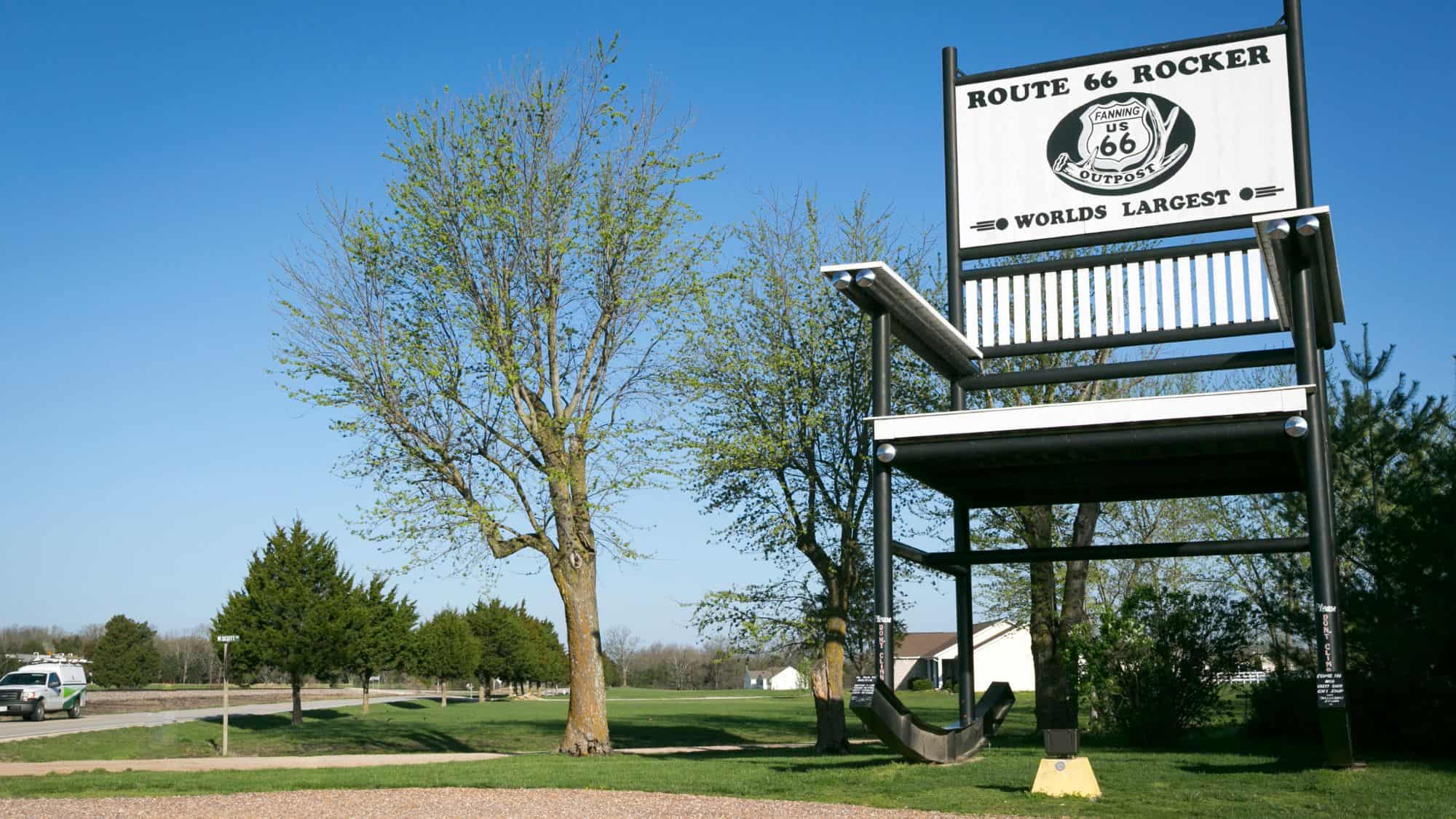 A gigantic black and white rocking chair, labeled “Route 66 Rocker” and “World’s Largest,” standing tall in an open field with trees and a clear blue sky. The oversized chair is a quirky roadside attraction along historic Route 66.