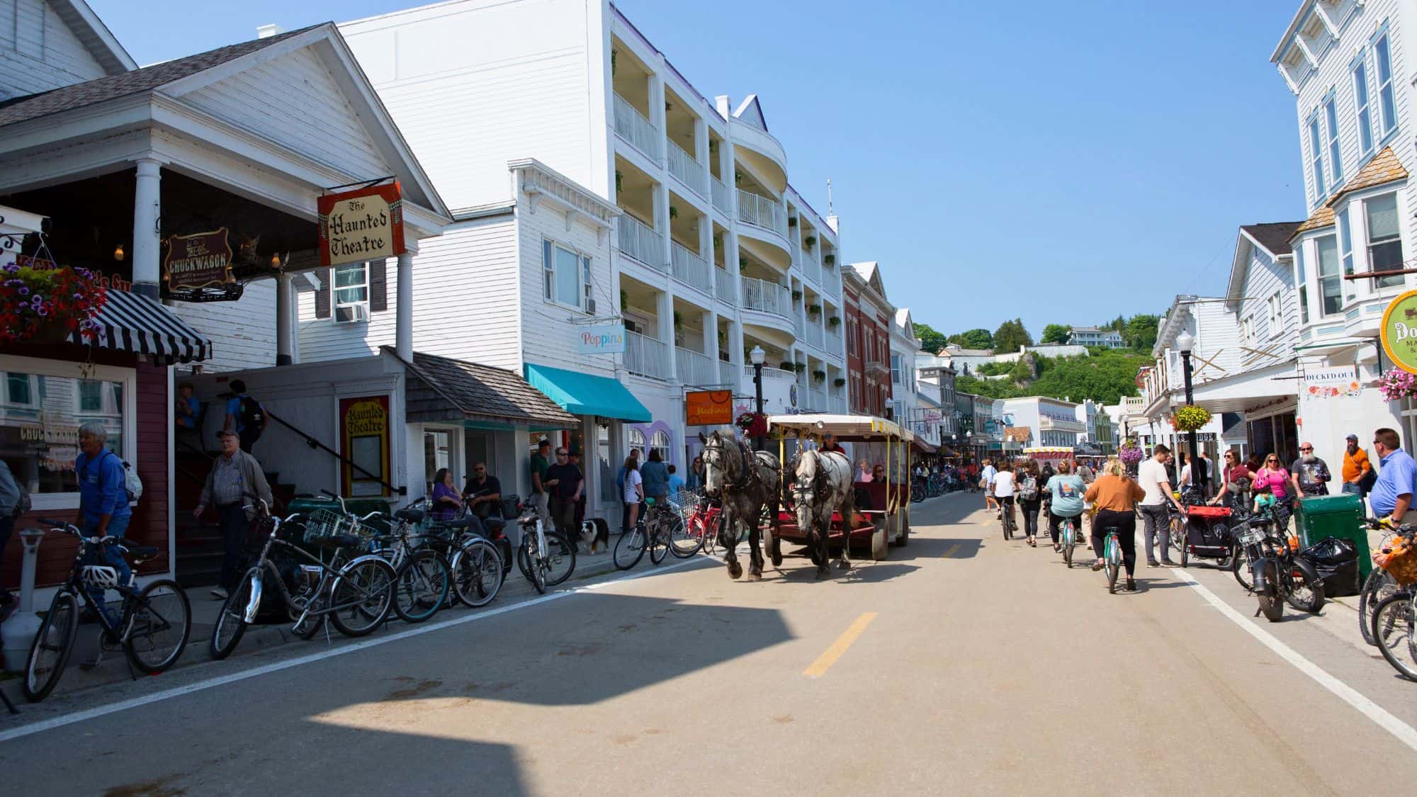 A bustling downtown street on Mackinac Island, filled with bicycles and a horse-drawn carriage. Quaint shops and historic buildings create a nostalgic, car-free charm.