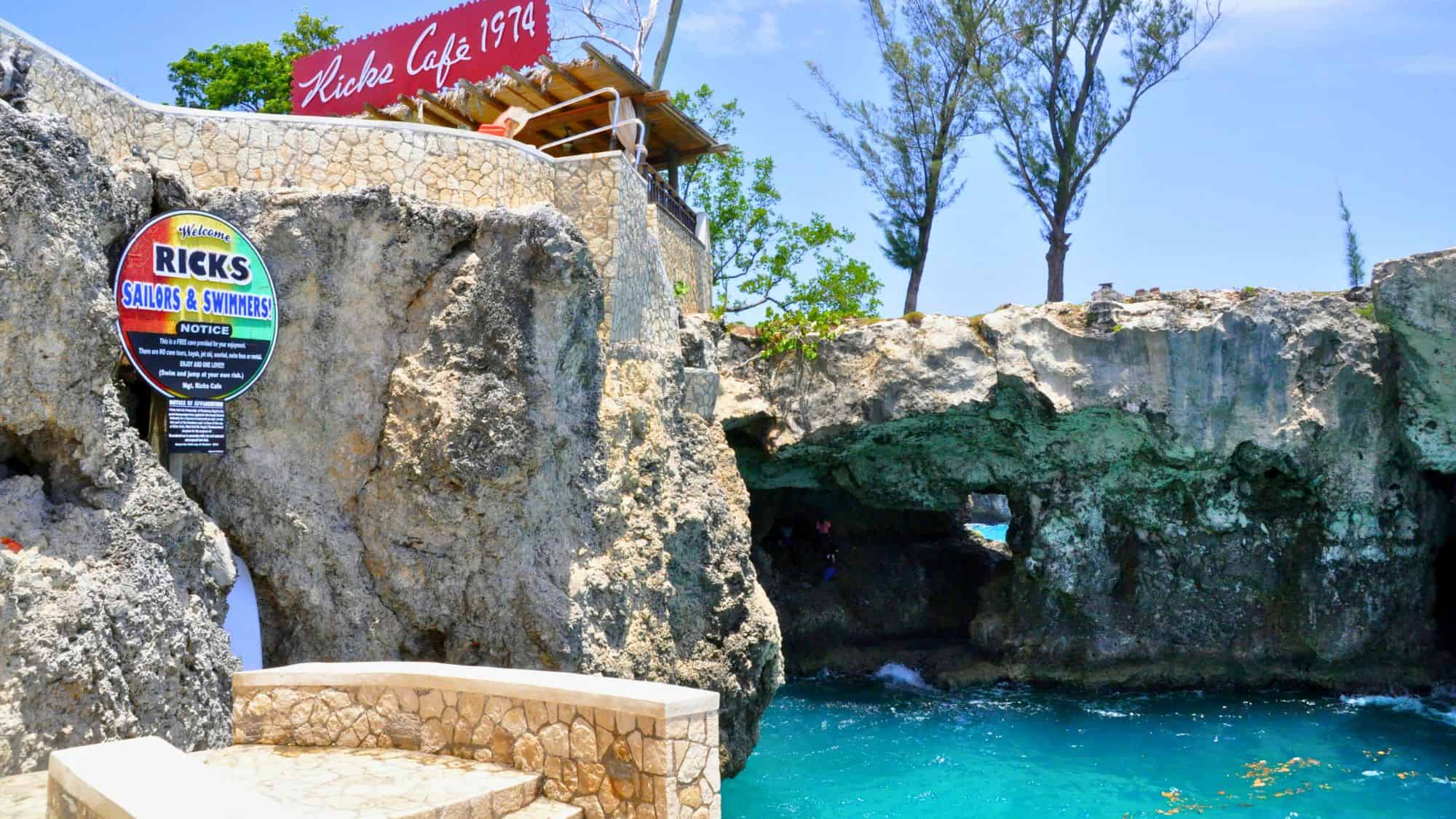 Rick’s Café in Negril, Jamaica, perched atop rocky cliffs overlooking the bright turquoise sea, invites visitors for cliff diving and scenic views.