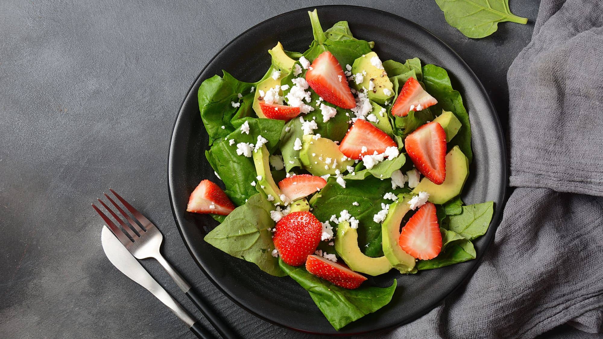 A fresh spinach salad topped with juicy strawberry slices, crumbled blue cheese, and crunchy walnuts. The salad is served on a black plate with whole strawberries scattered around.