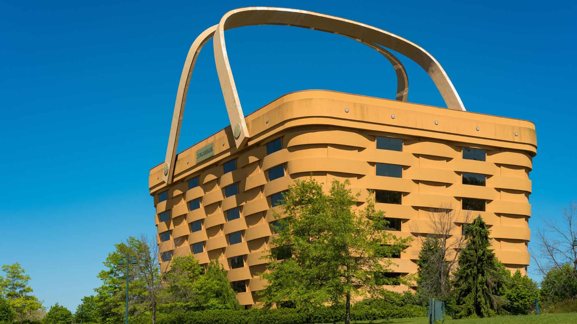 A massive, basket-shaped building with large handles extending above its roof, surrounded by green trees under a clear blue sky. This former headquarters of the Longaberger Basket Company is one of the most unique architectural landmarks in Ohio.